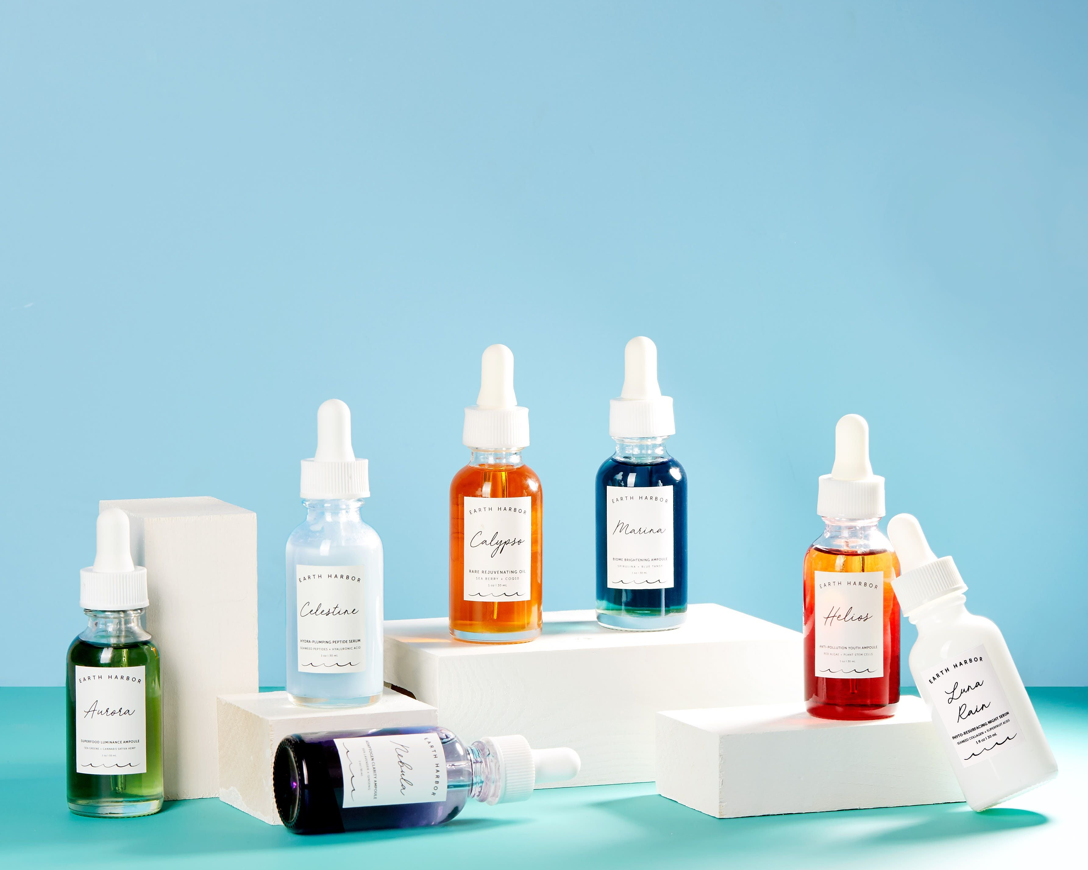 Vibrant collection of colorful dropper bottles on white blocks, featuring various skincare serums against a blue background.