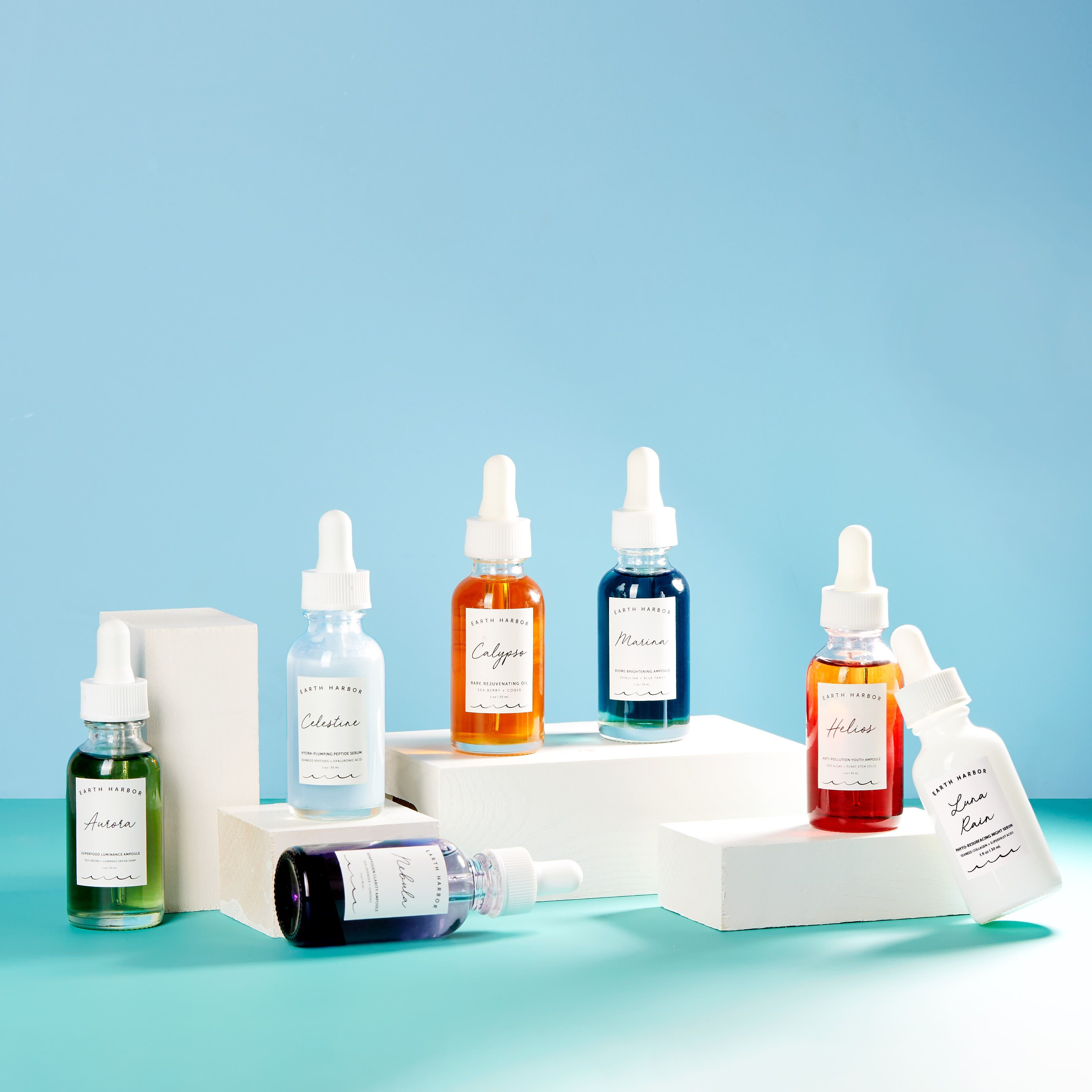 Vibrant collection of colorful dropper bottles on white blocks, featuring various skincare serums against a blue background.