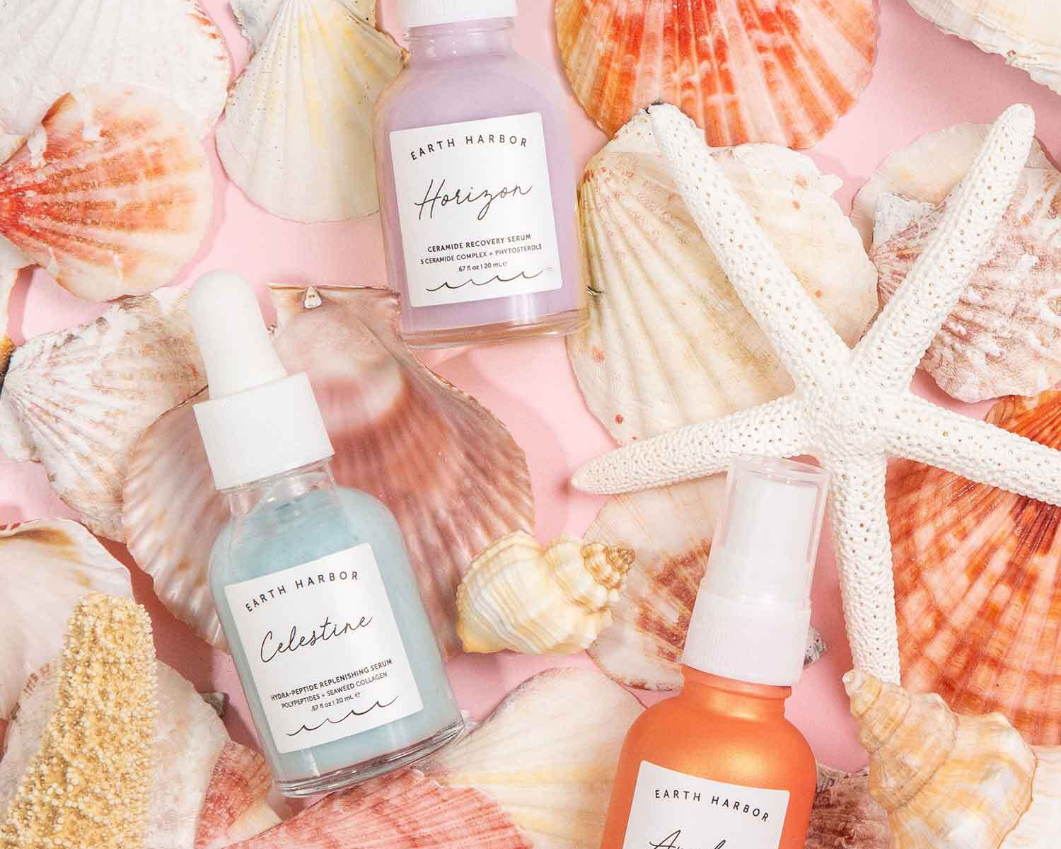 Three Earth Harbor skincare bottles in pastel colors, surrounded by various seashells and a white starfish.