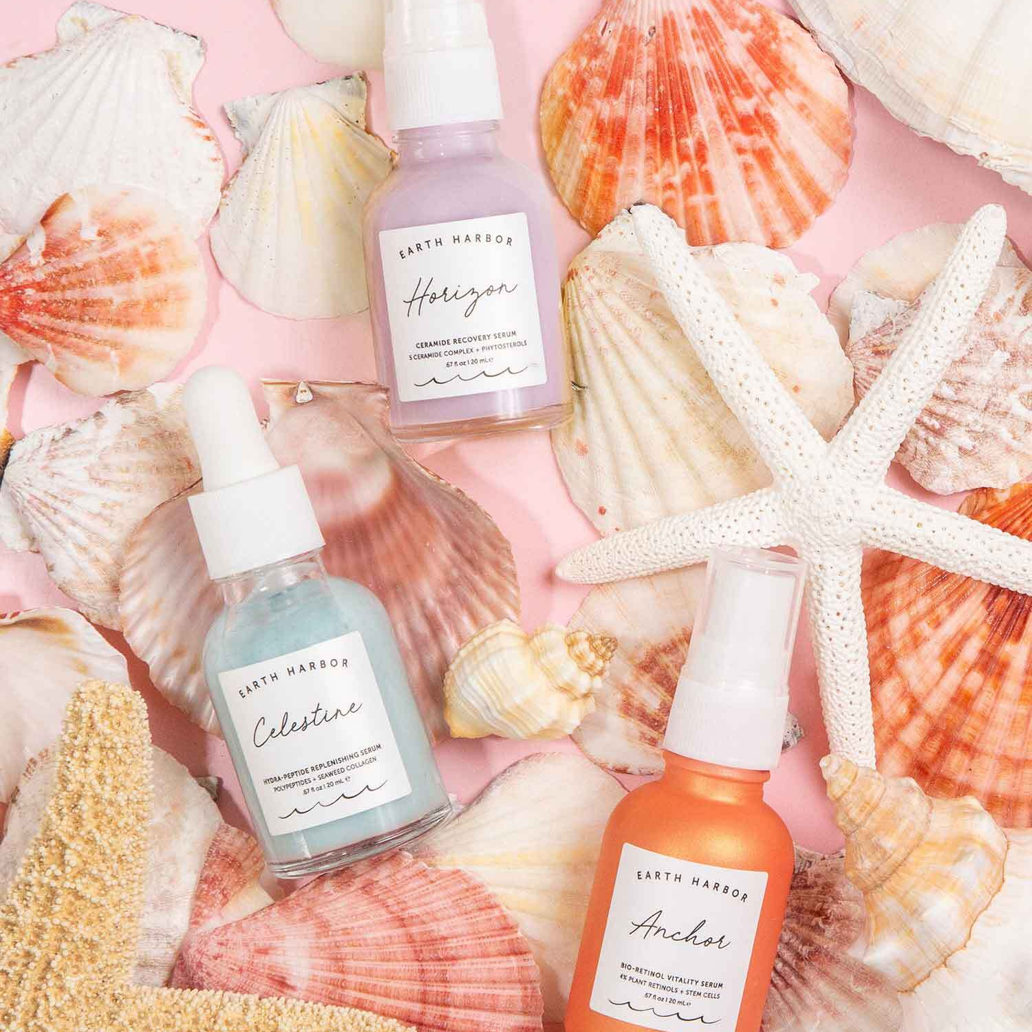Three Earth Harbor skincare bottles in pastel colors, surrounded by various seashells and a white starfish.