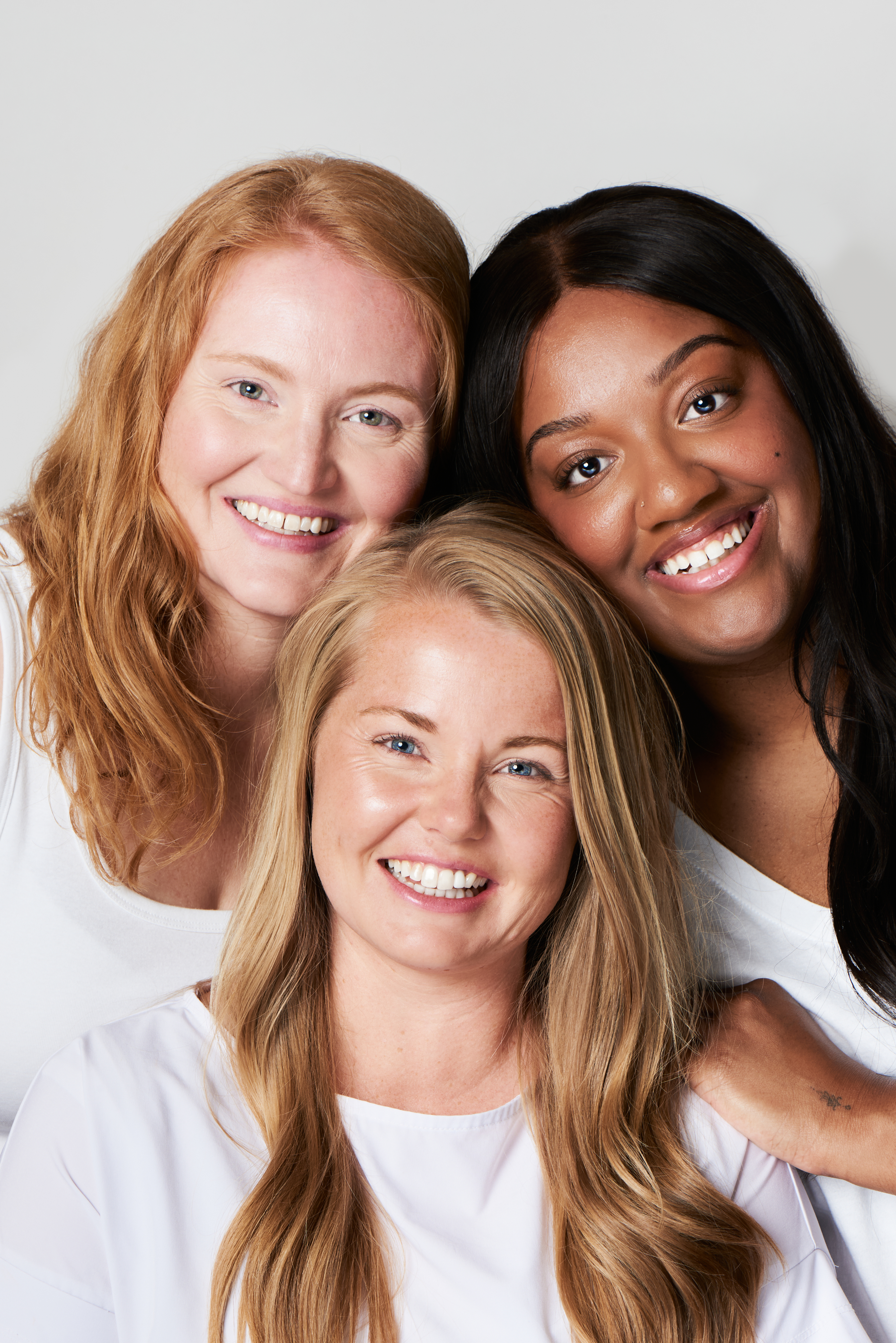 Close-up of three smiling women of
diverse backgrounds posing together happily.​