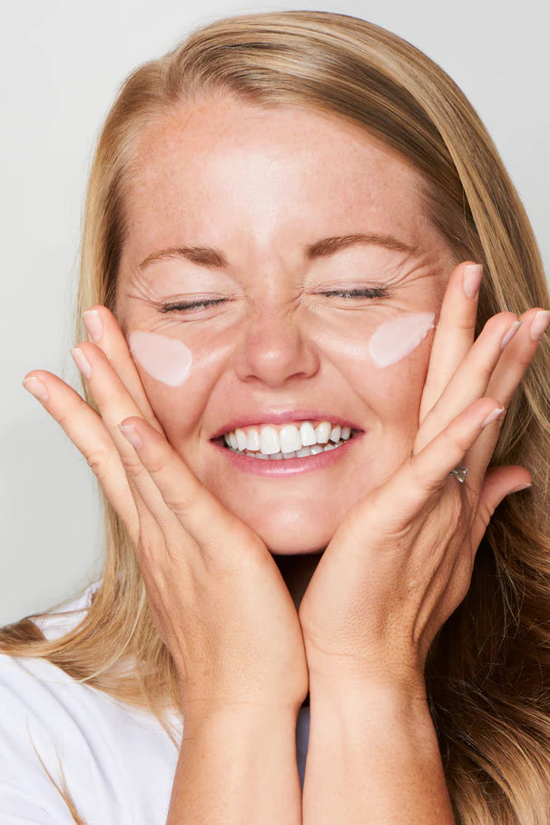 Smiling woman applying skincare cream
with both hands on her cheeks.​