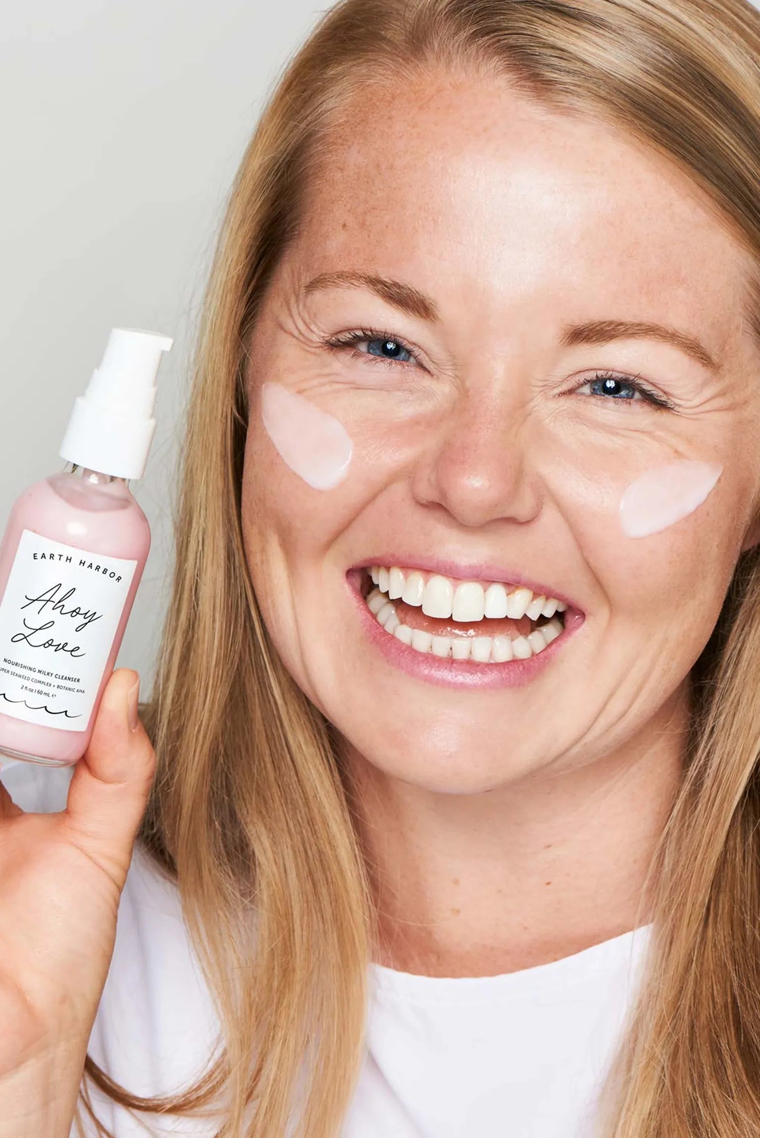 Smiling blonde woman holding Earth
Harbor Ahoy Love cleanser with pink
cream streaks on her cheeks.​
