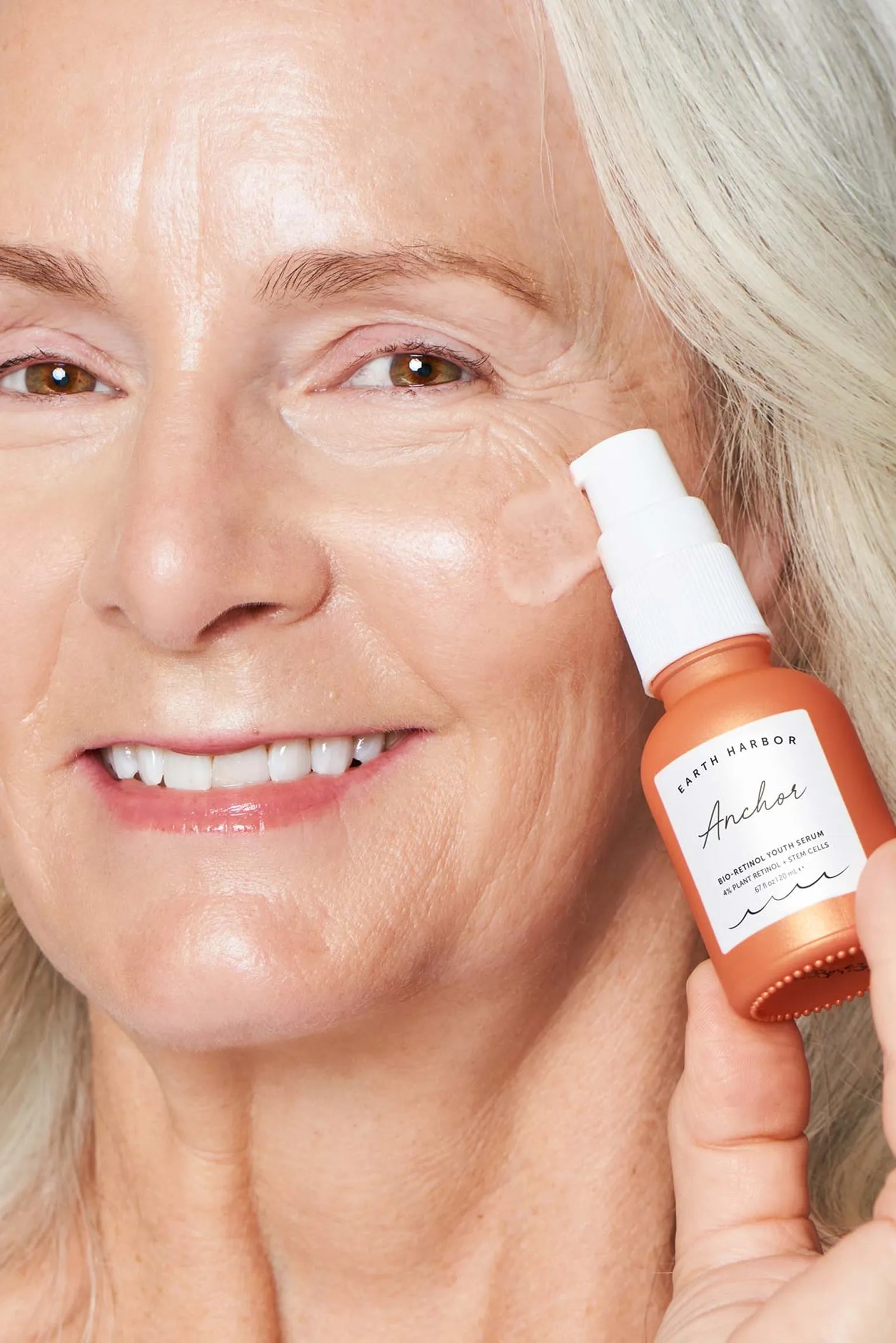 Smiling mature woman holding an orange
Earth Harbor Anchor serum bottle next to
her cheek.​