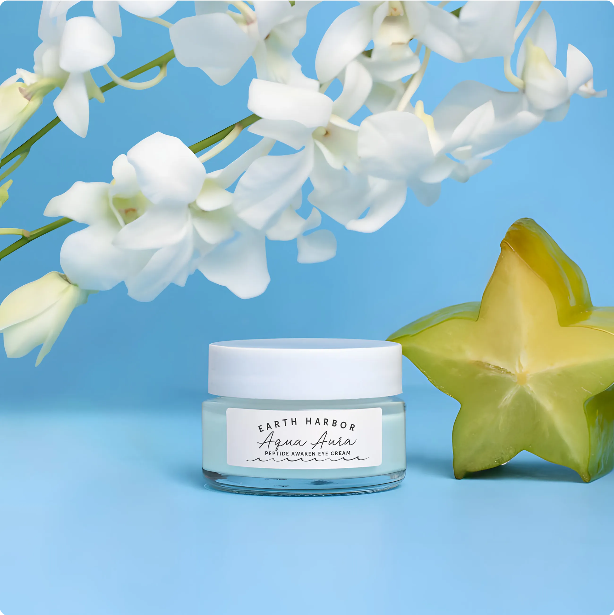 Earth Harbor Aqua Aura jar on a blue
background next to a starfruit slice and white
orchids.​