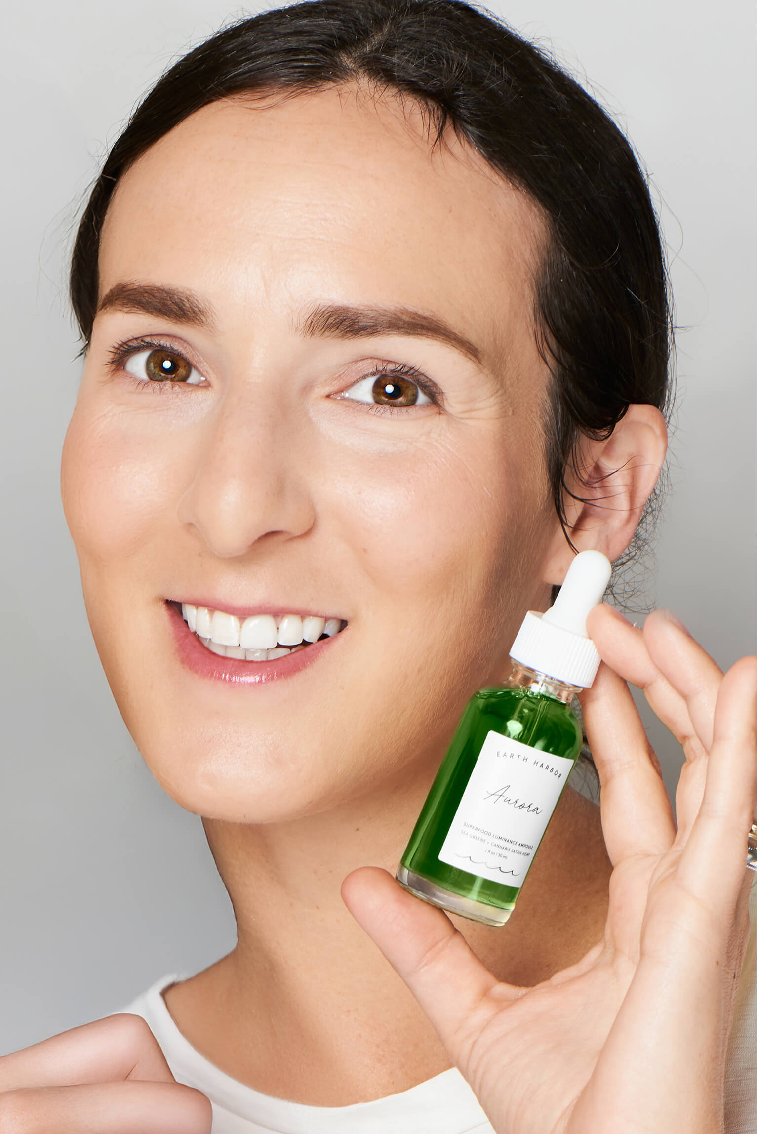 Smiling woman holding a green bottle of
Earth Harbor Aurora concentrate next to
her face.​