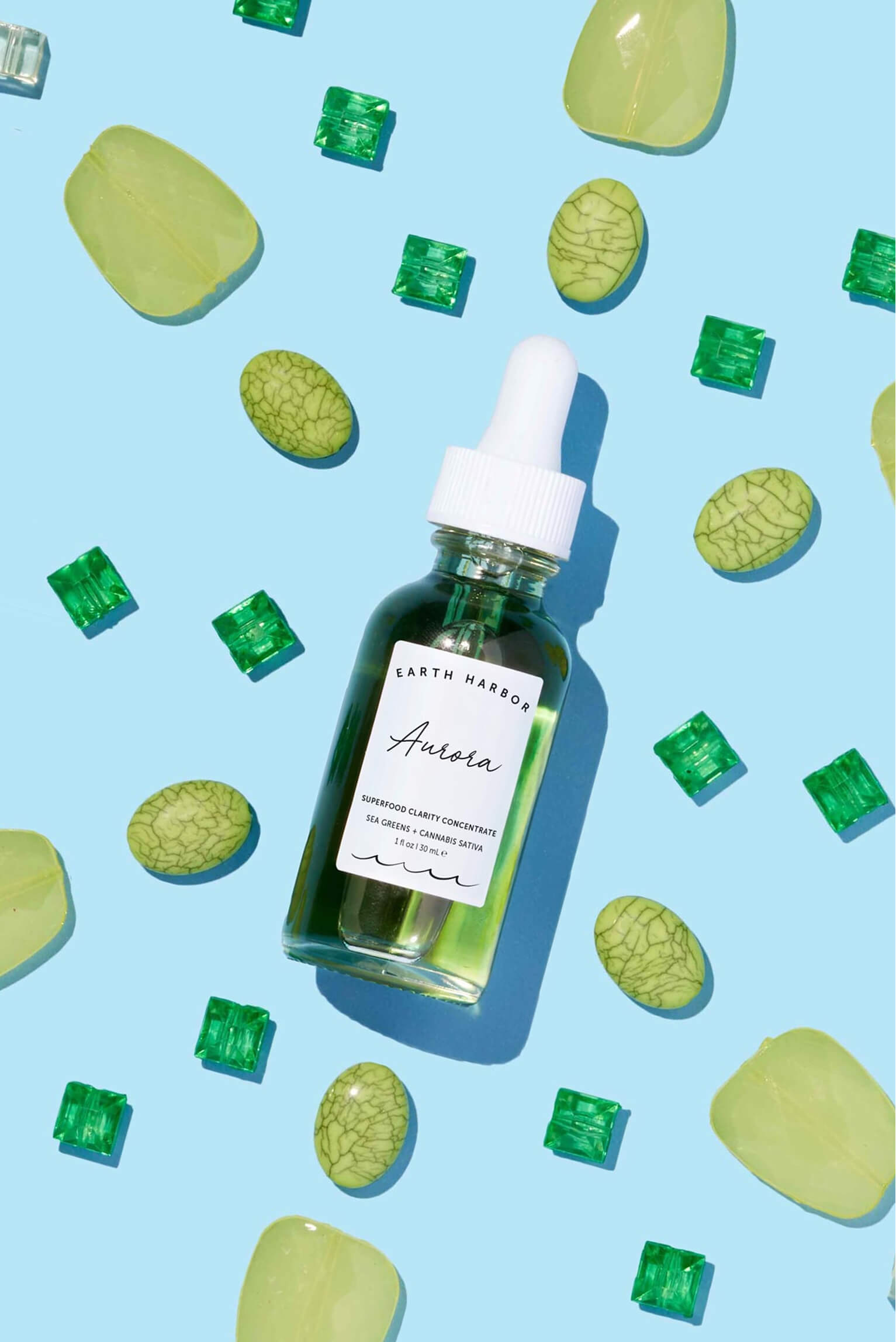Earth Harbor Aurora concentrate bottle
lying flat on a light blue background
patterned with green gemstones.​