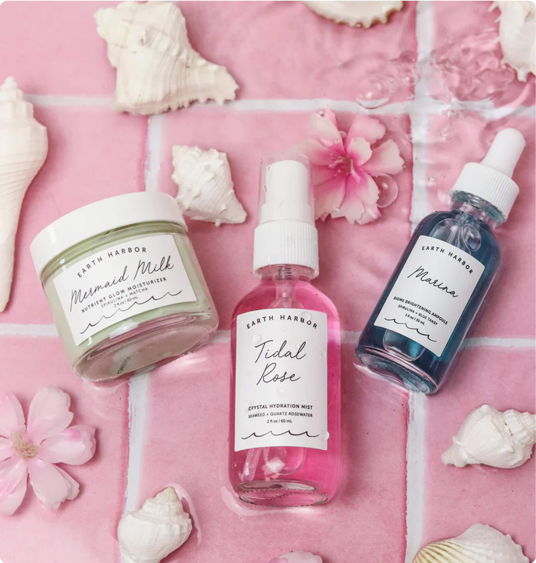Earth Harbor skincare products arranged on a pink tiled background with small white seashells and
pink flowers.​