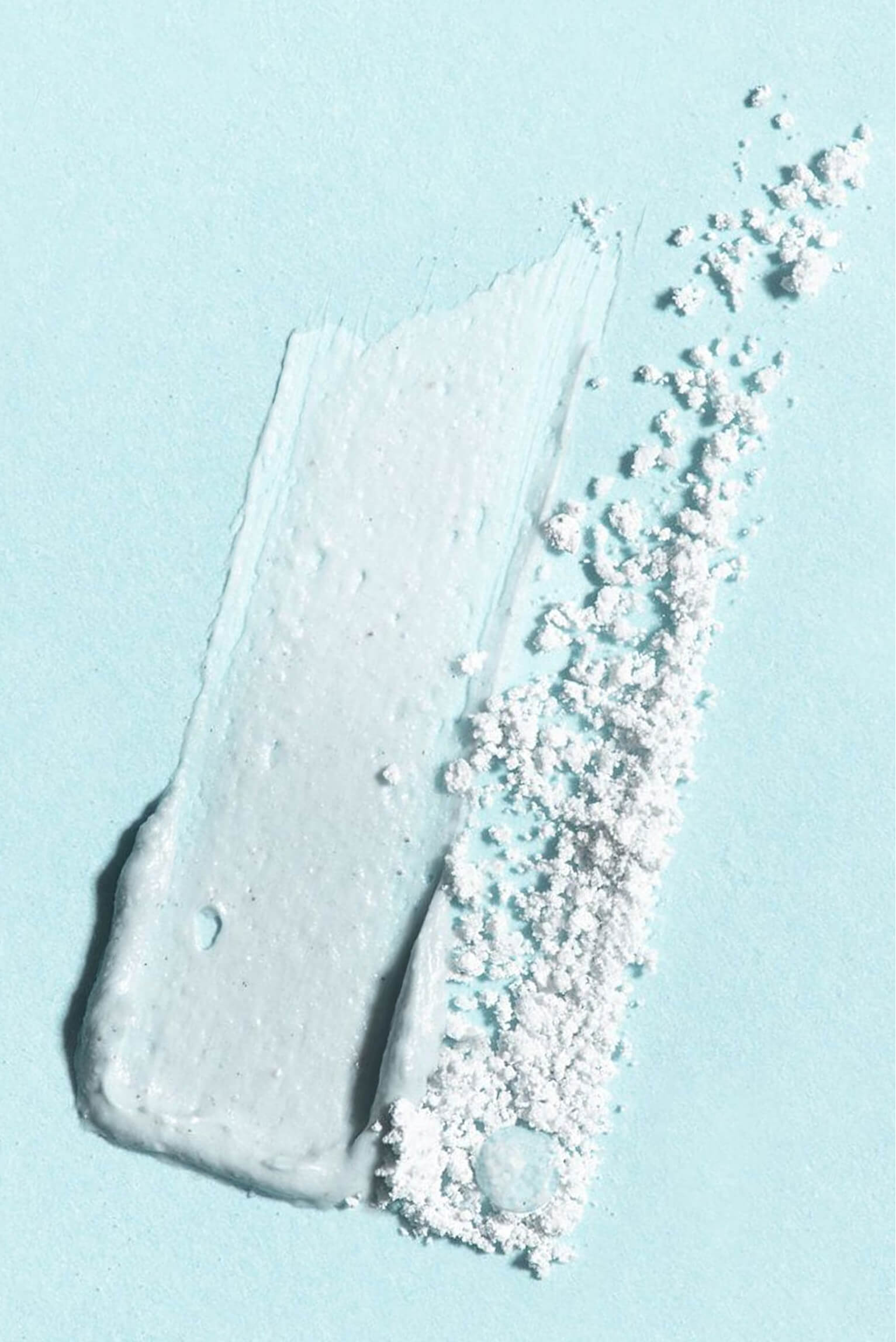 Smear of light blue cream mask next to
loose powder on a matching blue
background.​