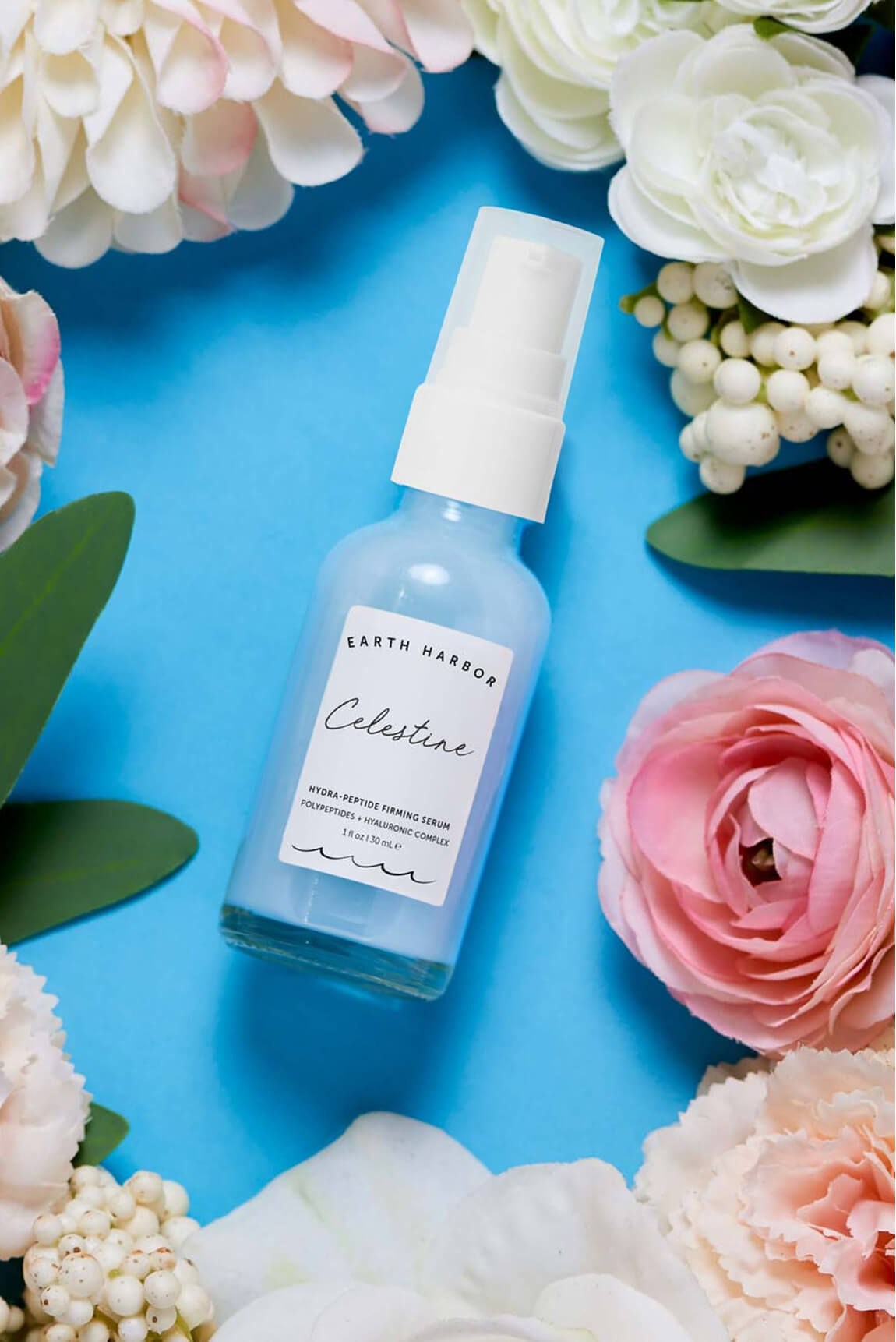 Earth Harbor Celestine serum bottle on a bright
blue background surrounded by pink and white
flowers.​
