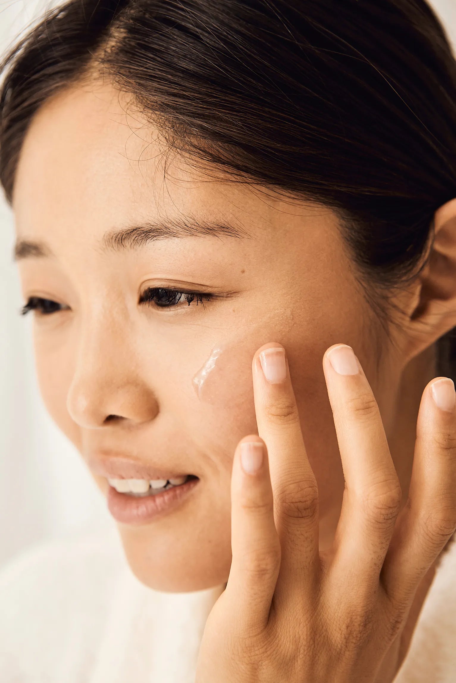 Woman gently applying a clear skincare
product onto her cheek with her
fingertips.​