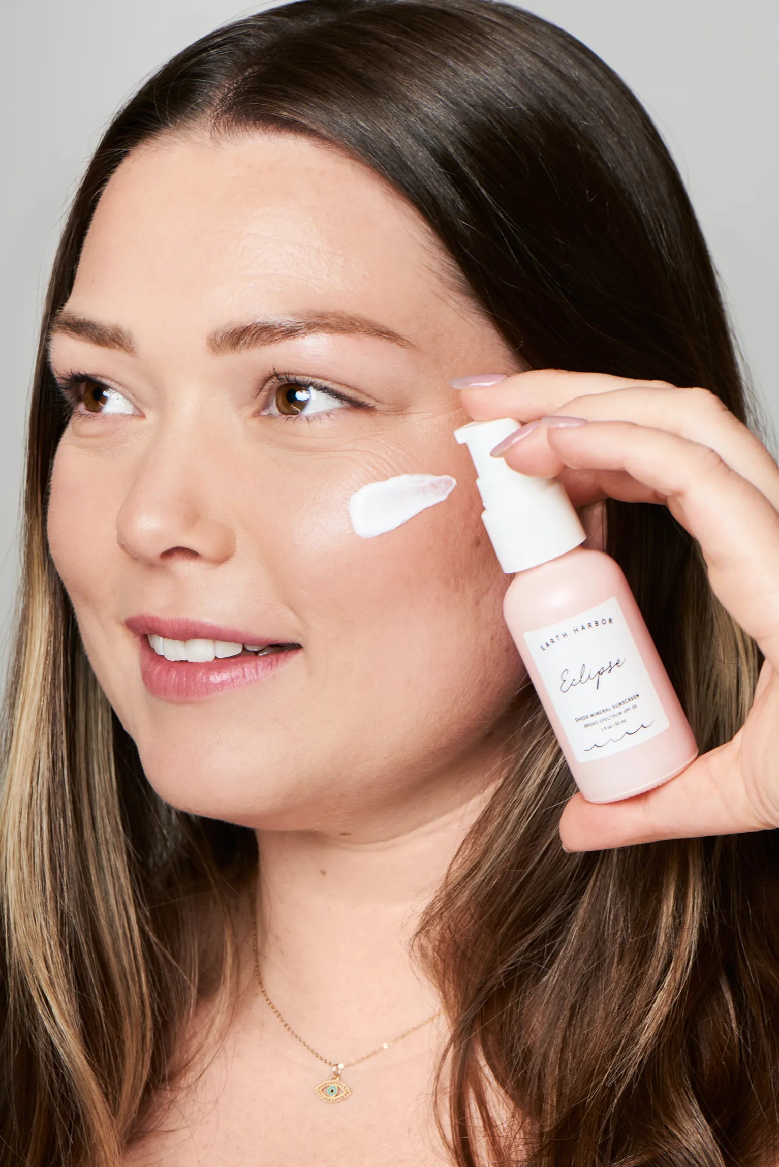 Smiling woman holding an Earth Harbor
Eclipse bottle with a streak of white
sunscreen on her cheek.​
