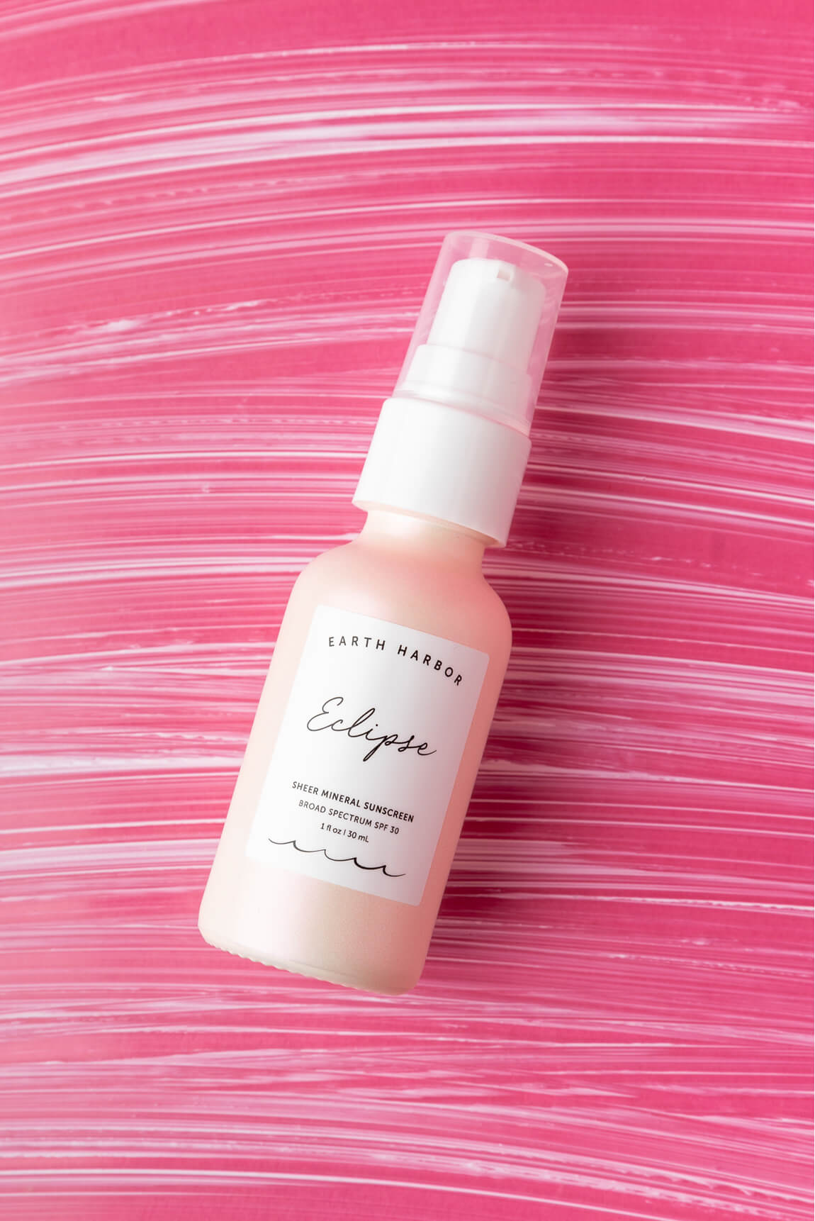 Earth Harbor Eclipse sunscreen bottle
laying flat on a vibrant, textured pink
background.​