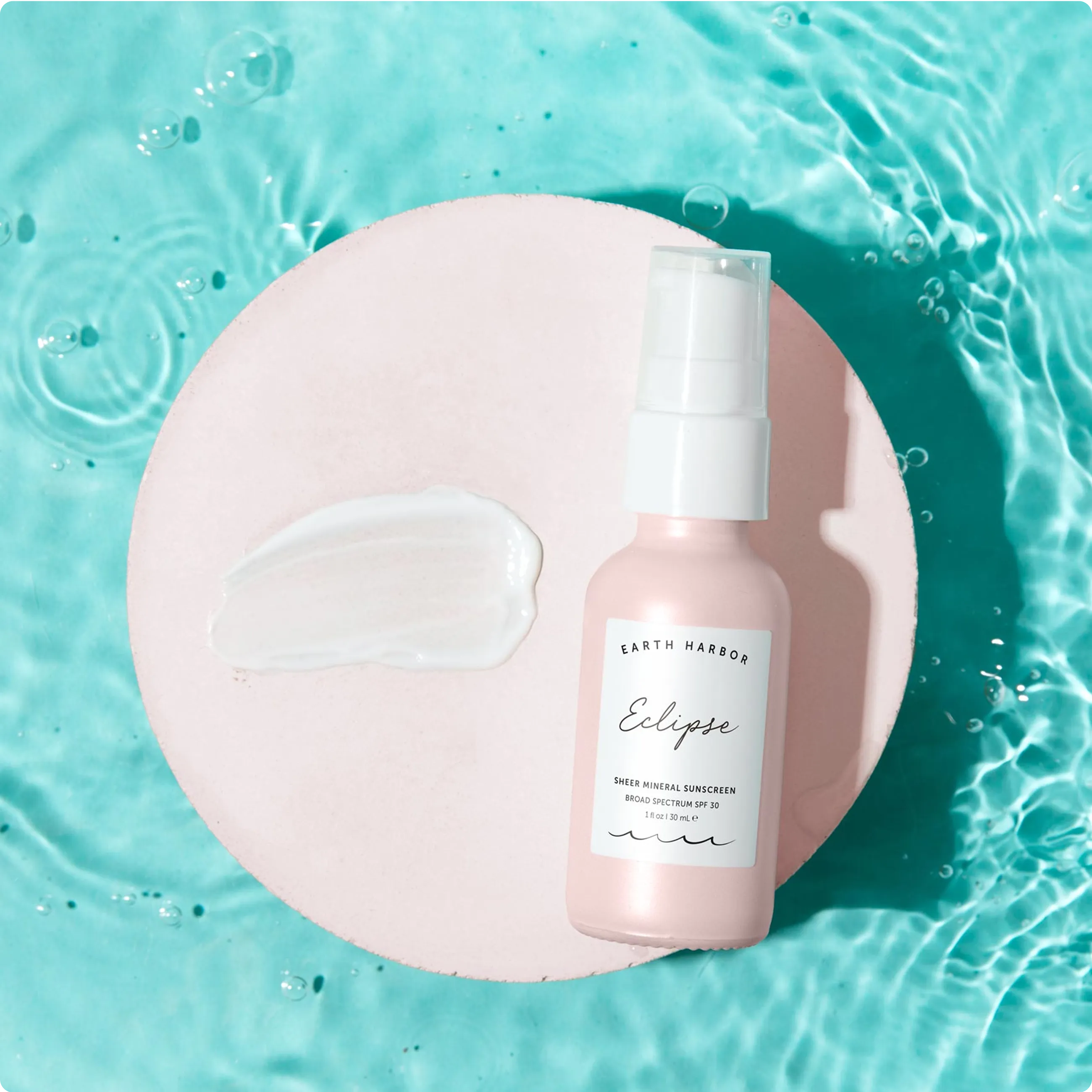 Earth Harbor Eclipse Sheer Mineral
Sunscreen bottle and a product swatch on
a pink disc in turquoise water.​