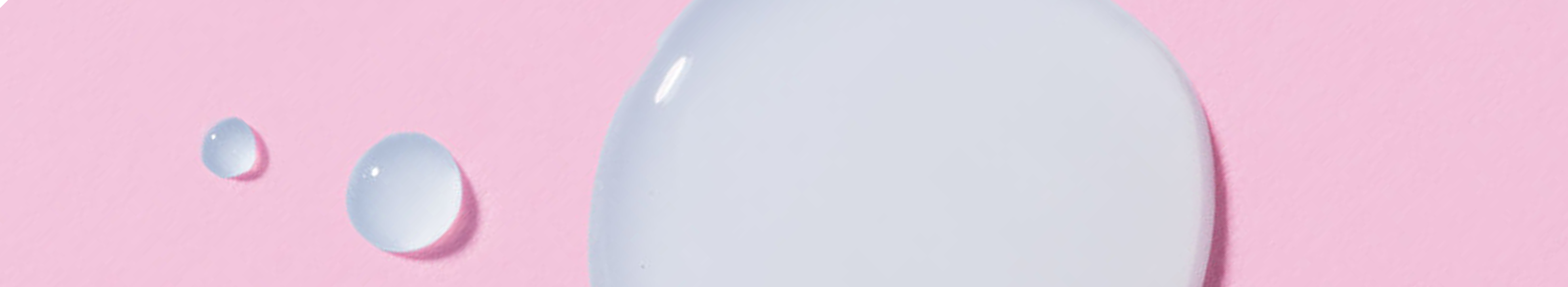 Close-up of clear skincare liquid droplets
on a pink background​