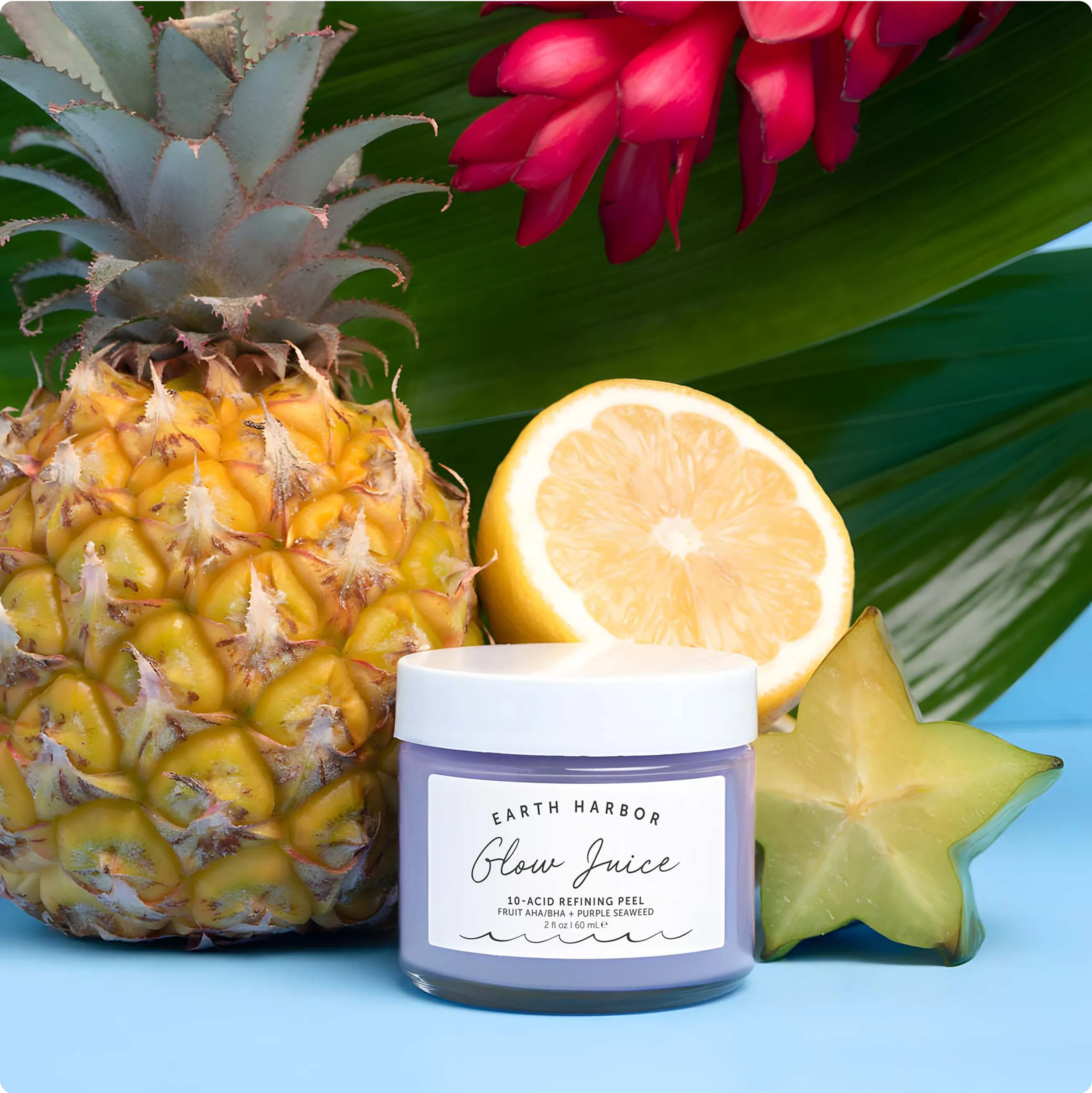 Jar of Earth Harbor Glow Juice mask in
clear, rippling blue water surrounded by
pink lily petals.​