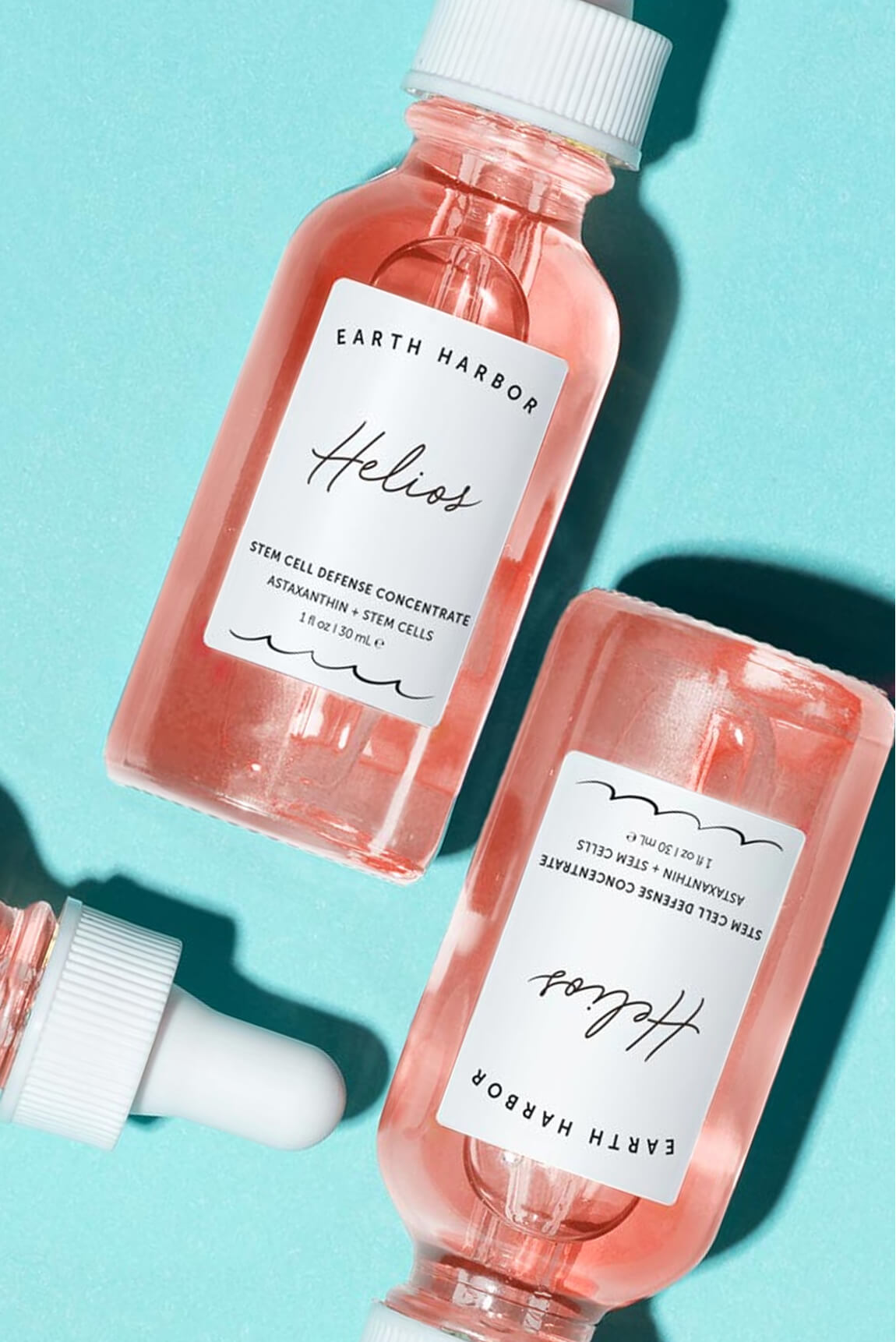 Two bottles of pink Earth Harbor Helios
concentrate lying flat on a bright turquoise
background.​