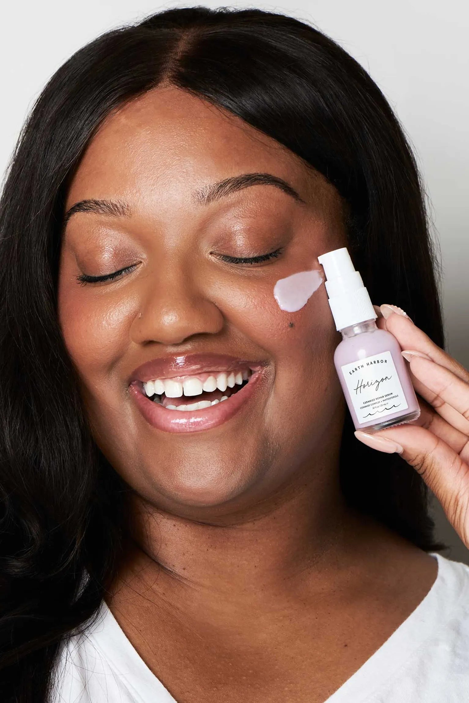 Smiling woman holding a purple Earth
Harbor Horizon serum bottle to her cheek.​