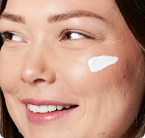 Woman applying a small amount of cream
to her cheek while smiling​