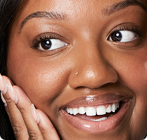 Smiling woman touching her cheek with
one hand, showing smooth skin.​