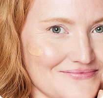  Woman with light skin smiling with a small
amount of cream applied to her cheek.