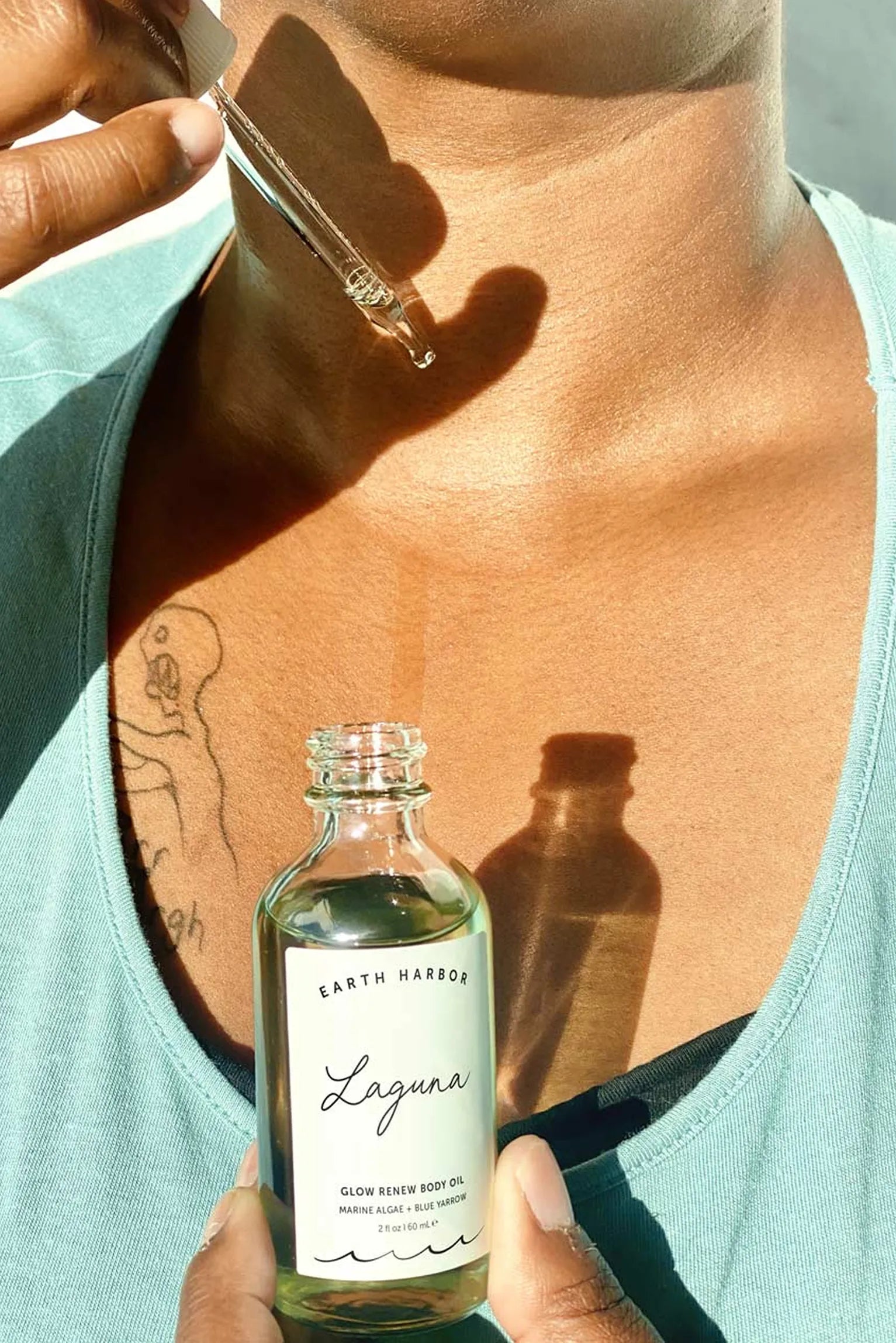 Person holding a dropper above their
collarbone with a bottle of Earth Harbor
Laguna body oil below.​
