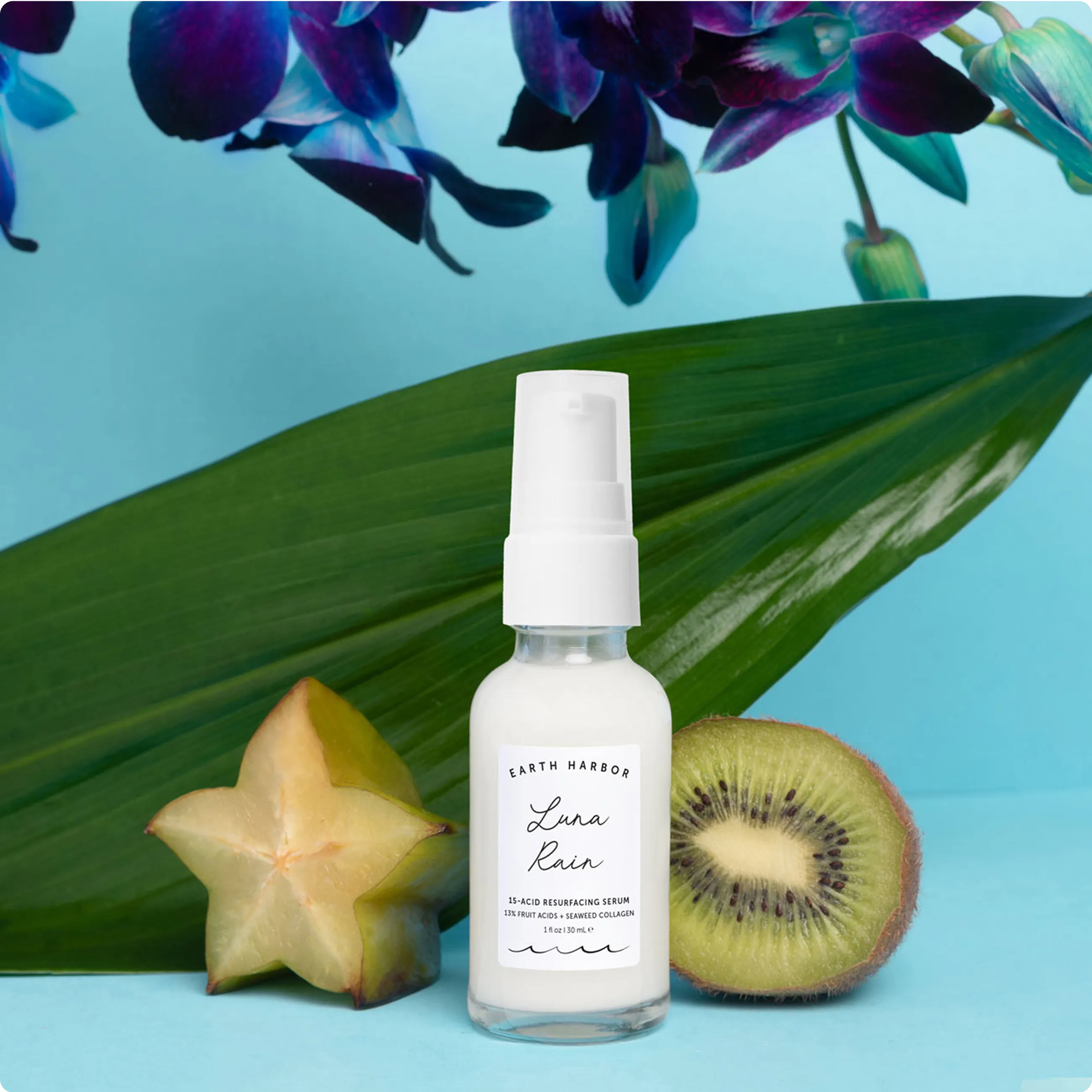 Earth Harbor Luna Rain serum bottle in
front of a palm leaf, a sliced starfruit, and a
kiwi half.​