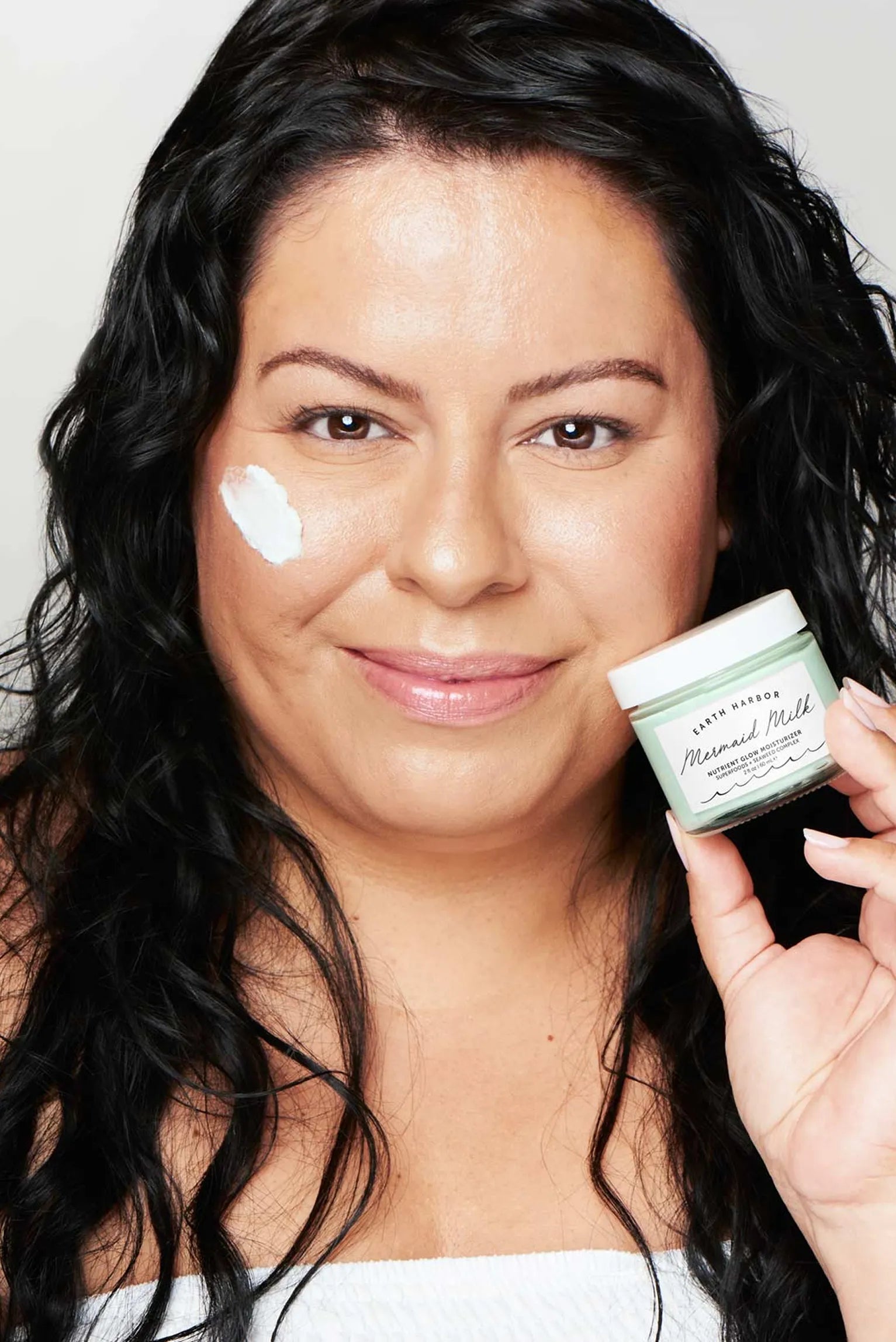 Smiling woman holding an Earth Harbor
Mermaid Milk jar with a swipe of cream on
her cheek.​