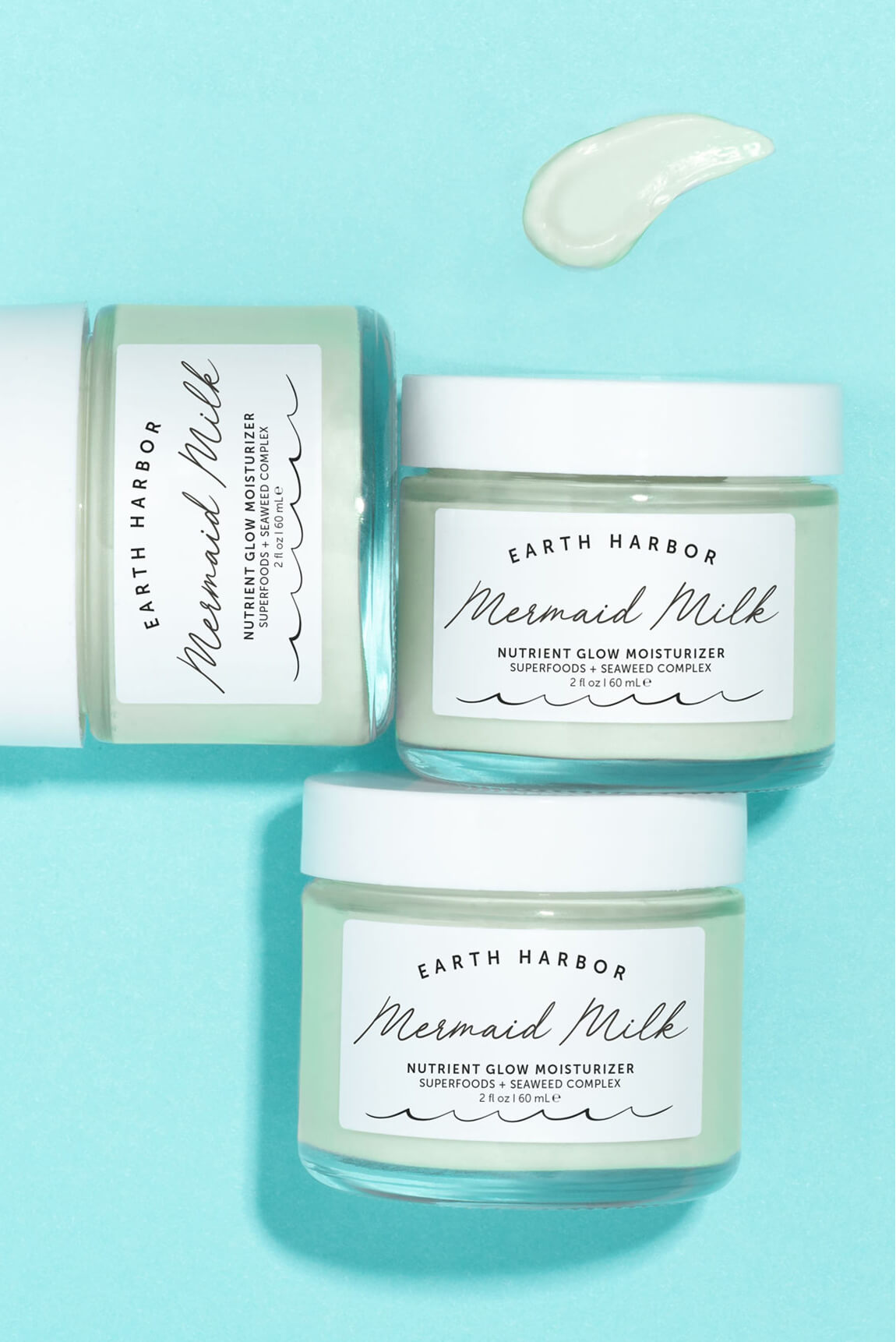 Three jars of Earth Harbor Mermaid Milk
moisturizer arranged on a light turquoise
background.​