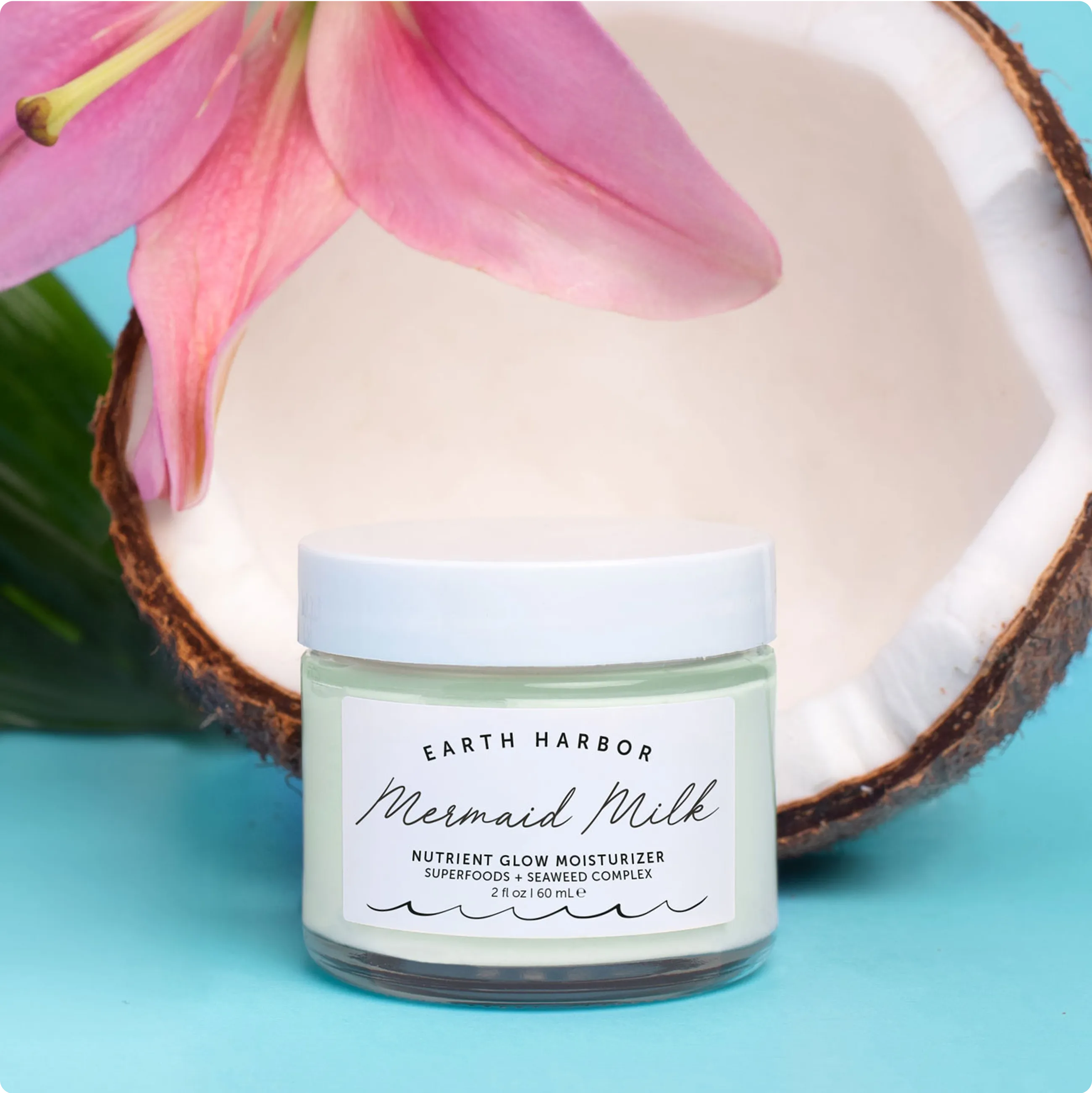 Earth Harbor Mermaid Milk moisturizer jar
placed in front of an open coconut half
with a pink flower.​