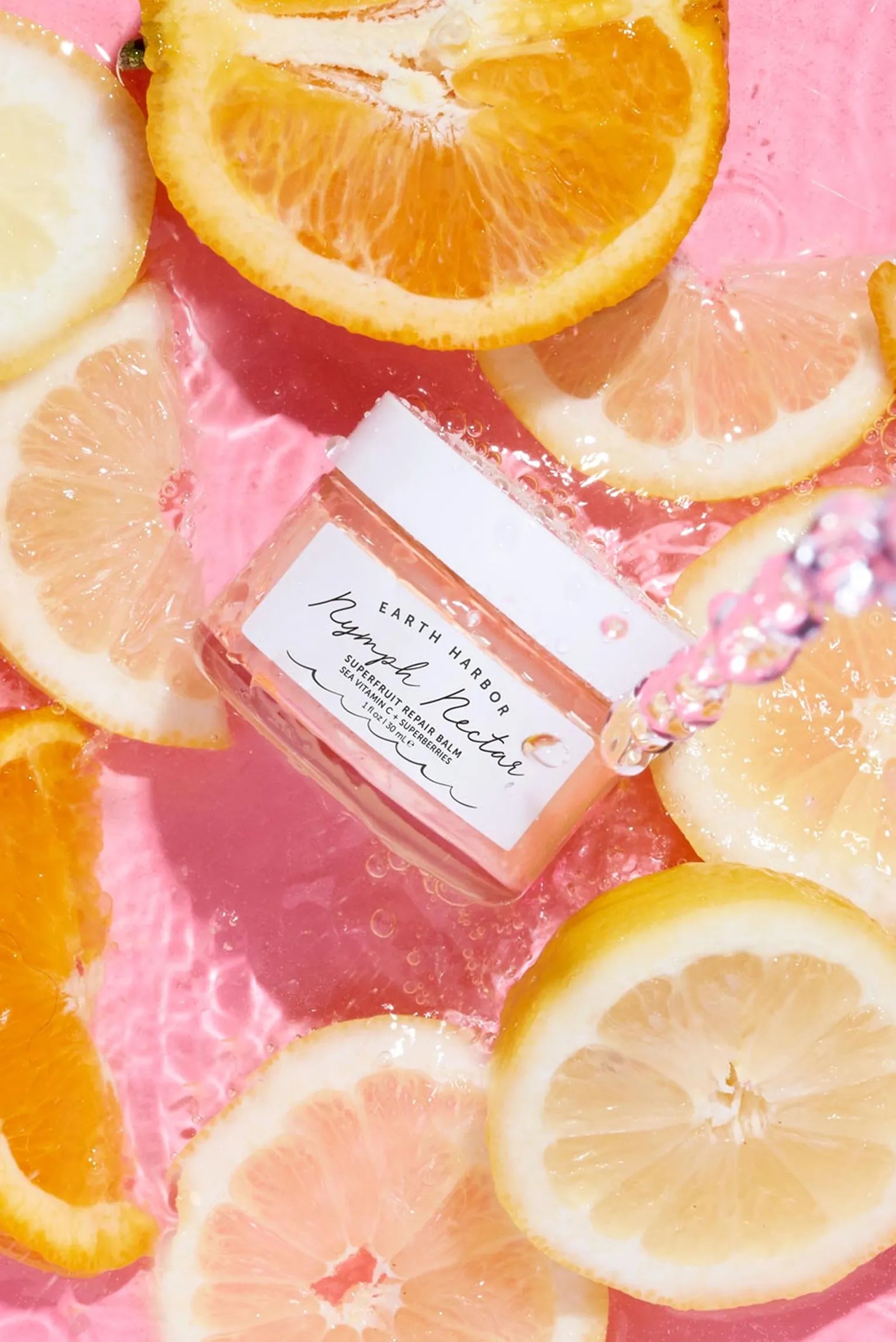 Earth Harbor Nymph Nectar jar surrounded by
orange and lemon slices splashing in pink water.​