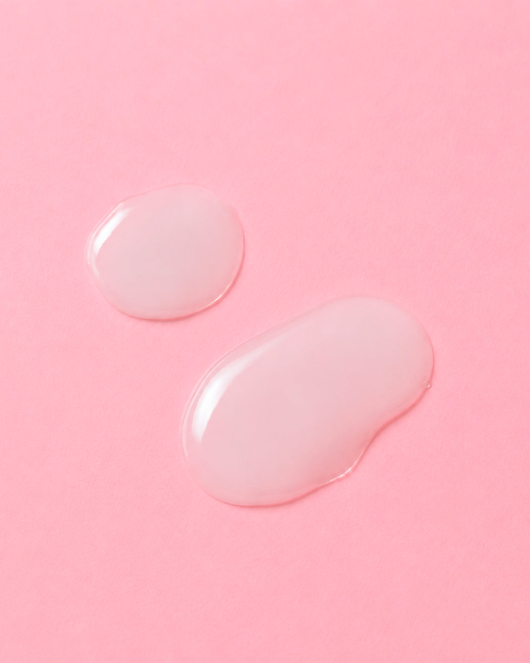 Two translucent, glossy droplets of a clear cosmetic gel or serum on a solid pink background.