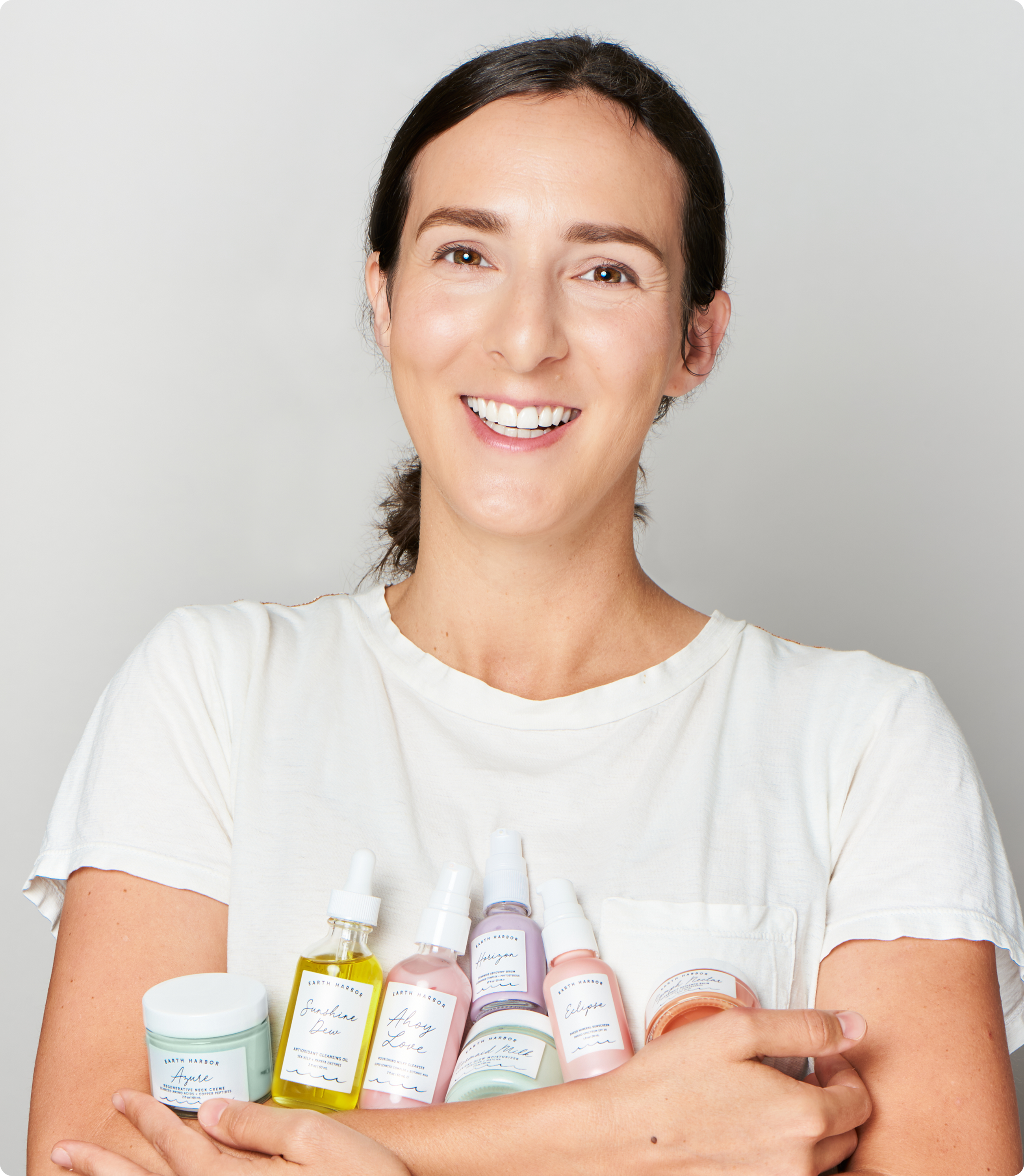 Smiling woman with brown hair wearing a white t-shirt against a neutral background.​