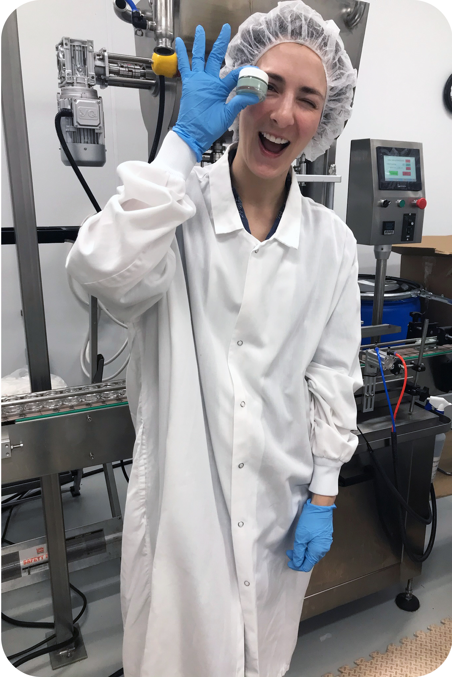 Smiling lab worker in protective gear
standing next to manufacturing equipment.