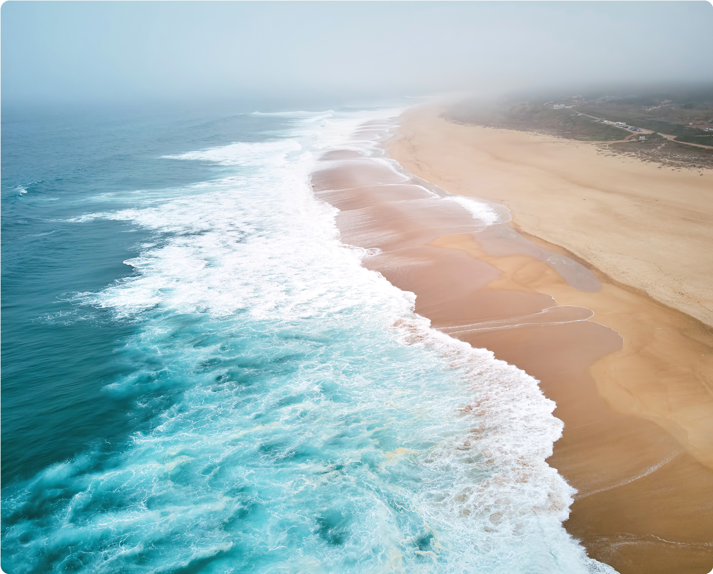 Aerial view of ocean waves meeting a
sandy beach coastline.​