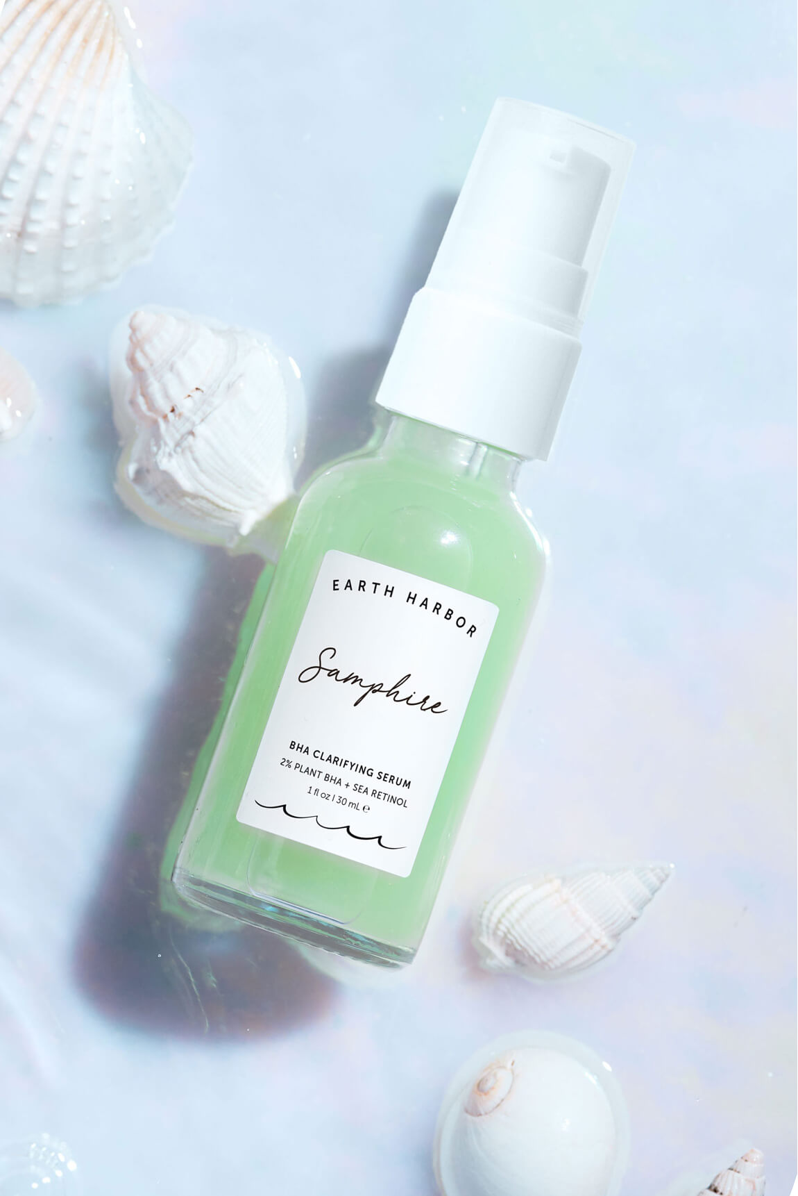 Earth Harbor Samphire serum bottle on a
light blue surface surrounded by white
seashells.​