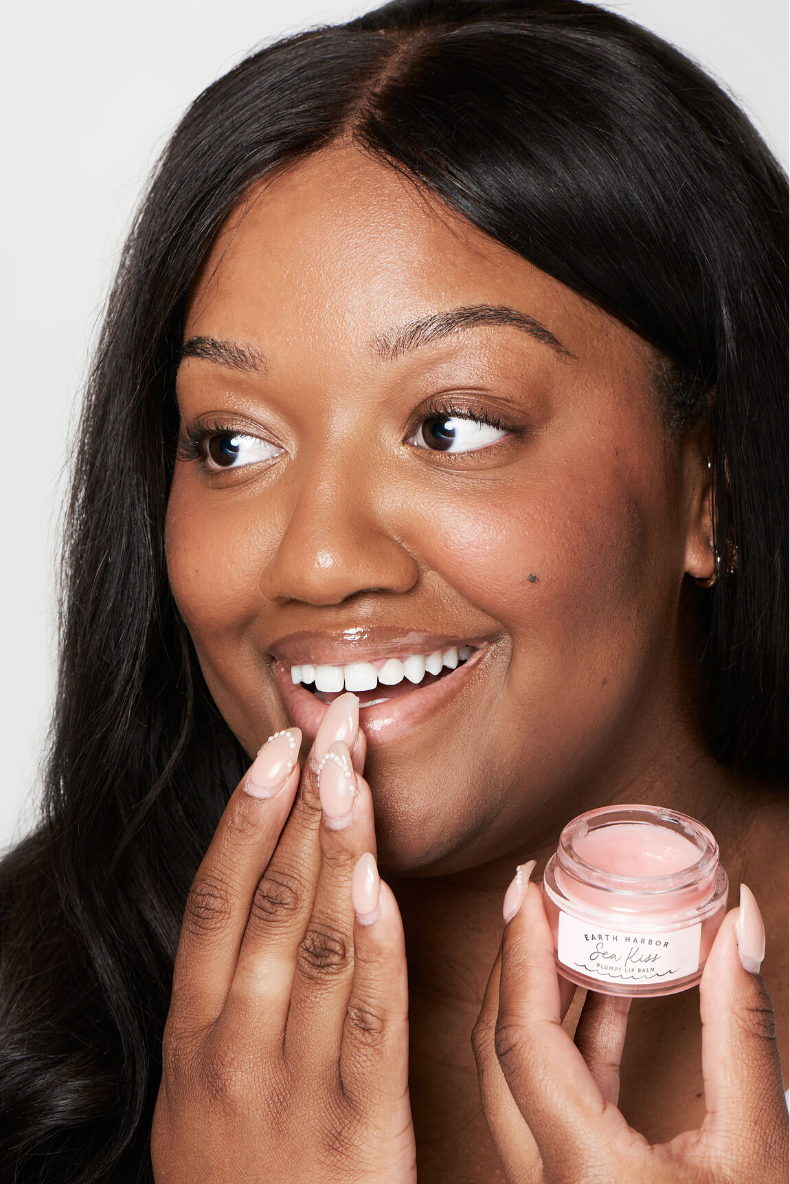Smiling woman applying lip balm from a
small pink Earth Harbor Sea Kiss jar.​