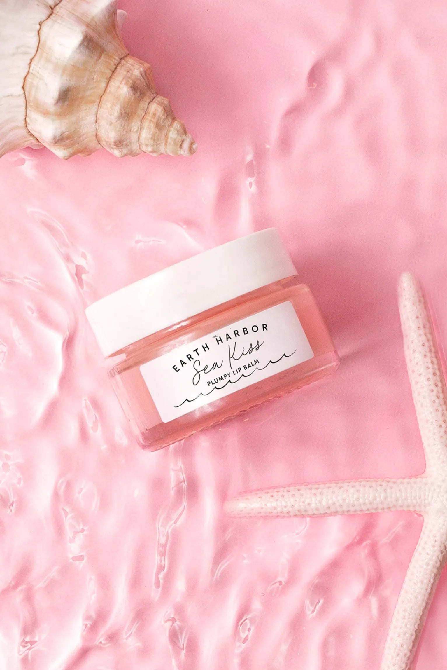 Earth Harbor Sea Kiss jar floating in pink
rippled water alongside a white starfish
and a seashell.​
