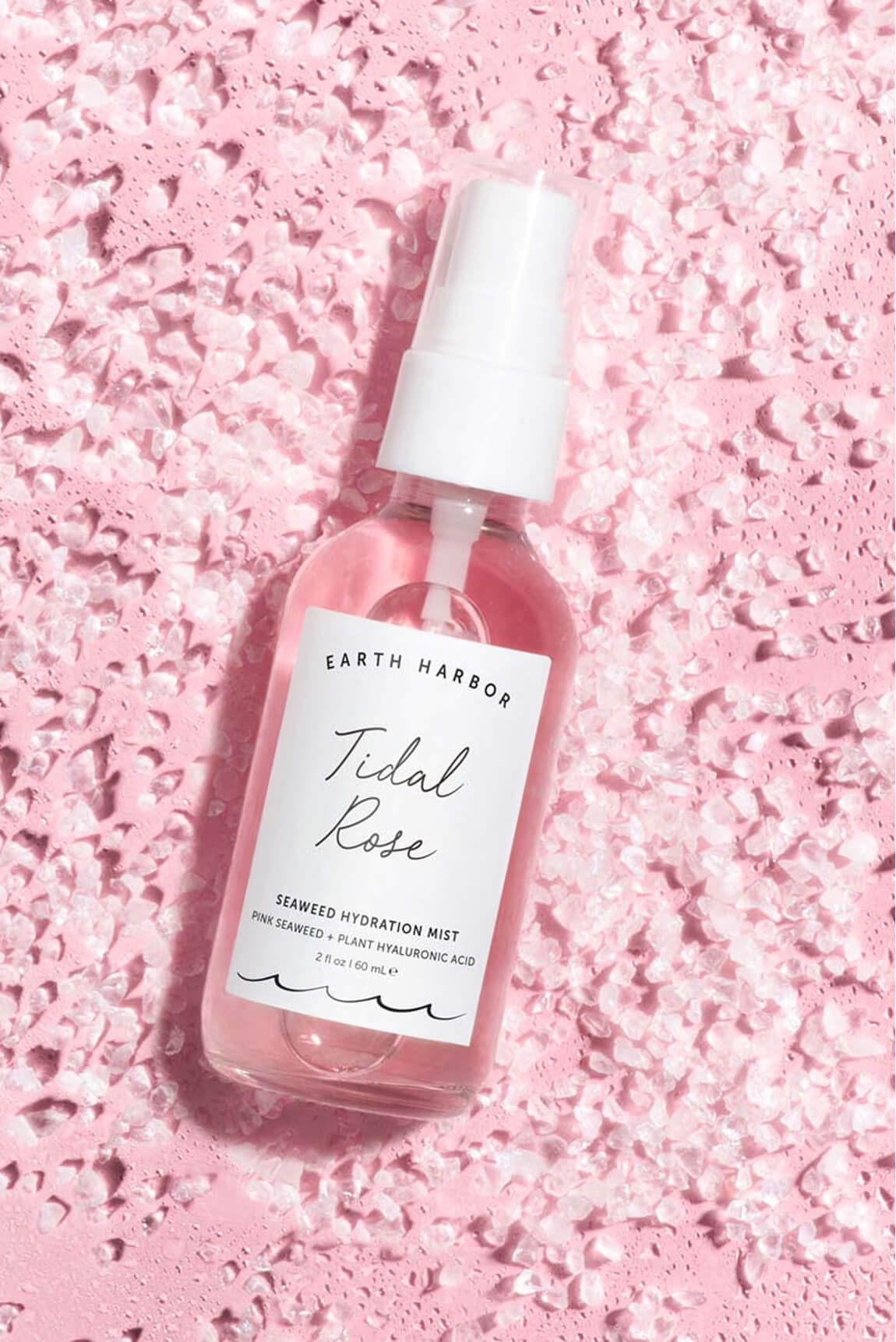 Earth Harbor Tidal Rose mist bottle laying
flat on a textured, light pink crystal or salt
background.​