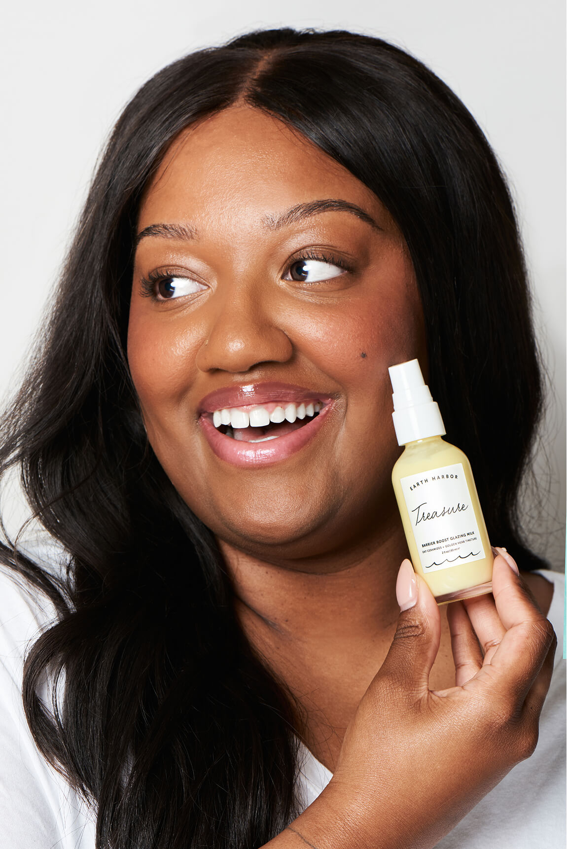 Smiling woman with long dark hair holding
an Earth Harbor Treasure bottle next to
her face.​