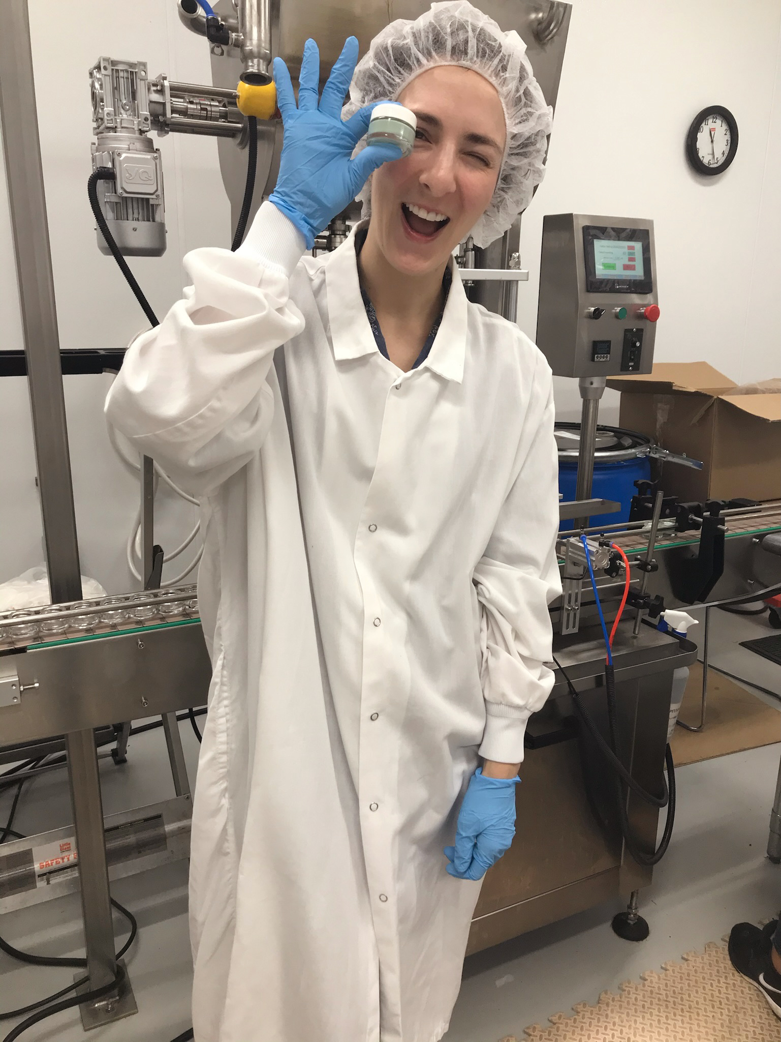 Smiling lab worker in protective gear
standing next to manufacturing equipment​