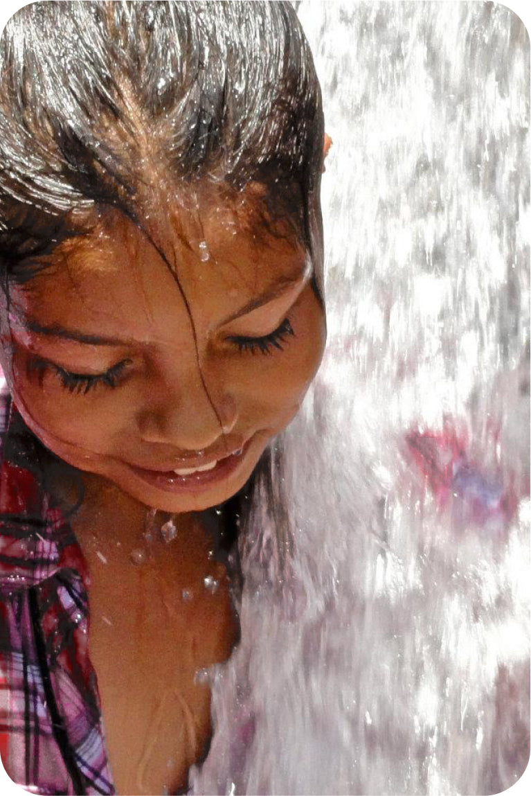 Young girl smiling with water splashing
over her face outdoors.​