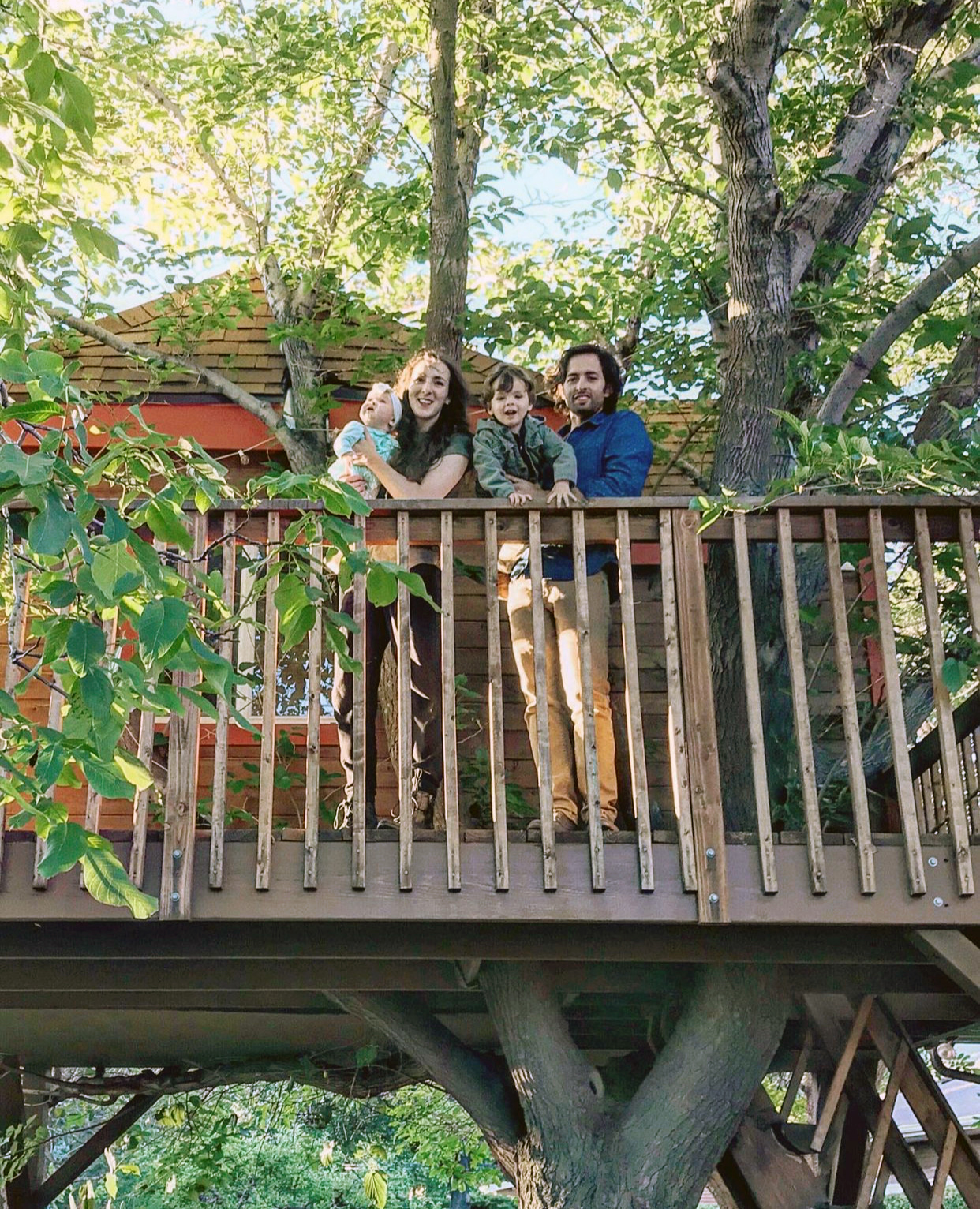 Family standing on a wooden treehouse
deck surrounded by trees.​
