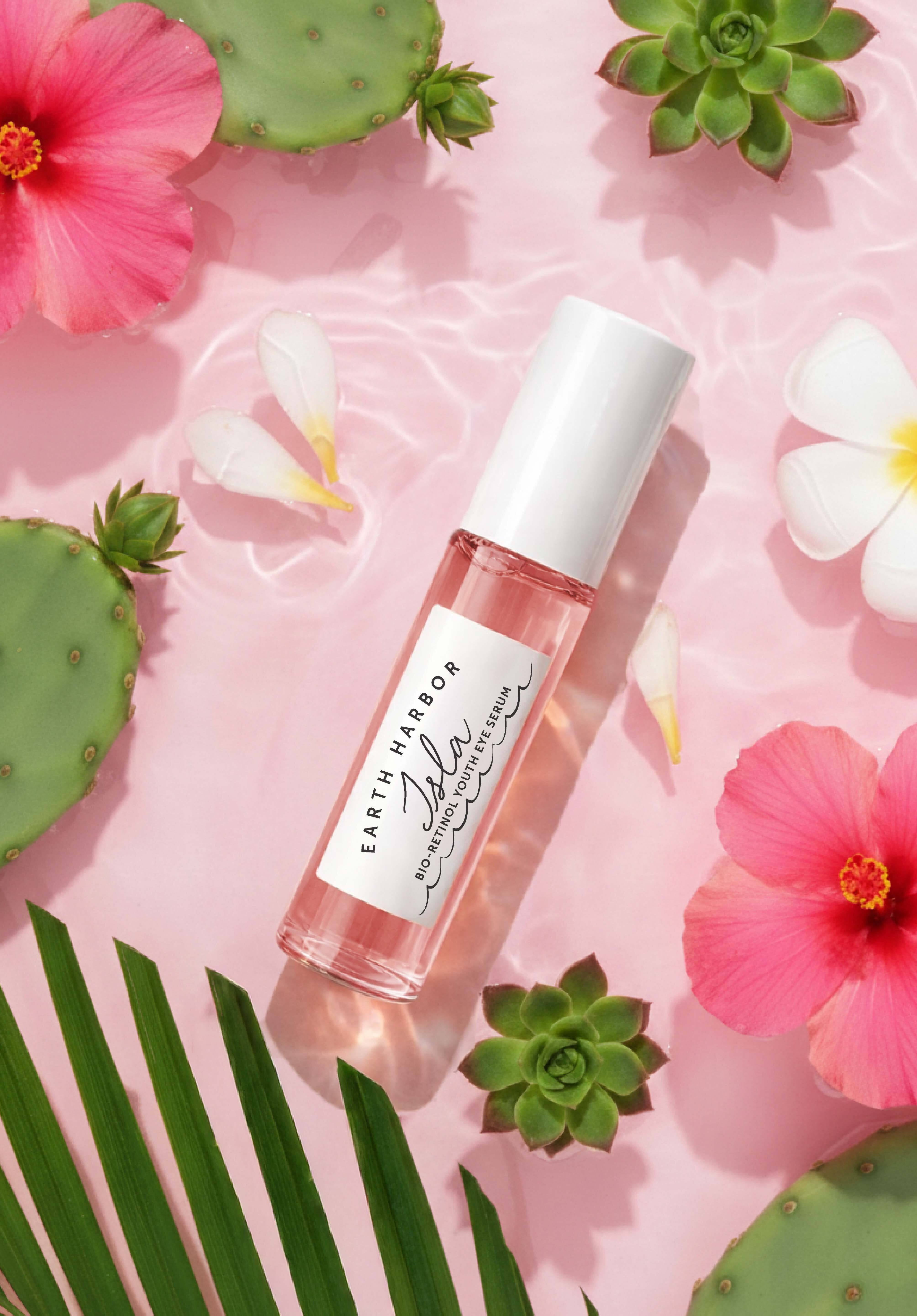 Pink Isla serum bottle surrounded by
tropical flowers and greenery on a soft pink
background.​