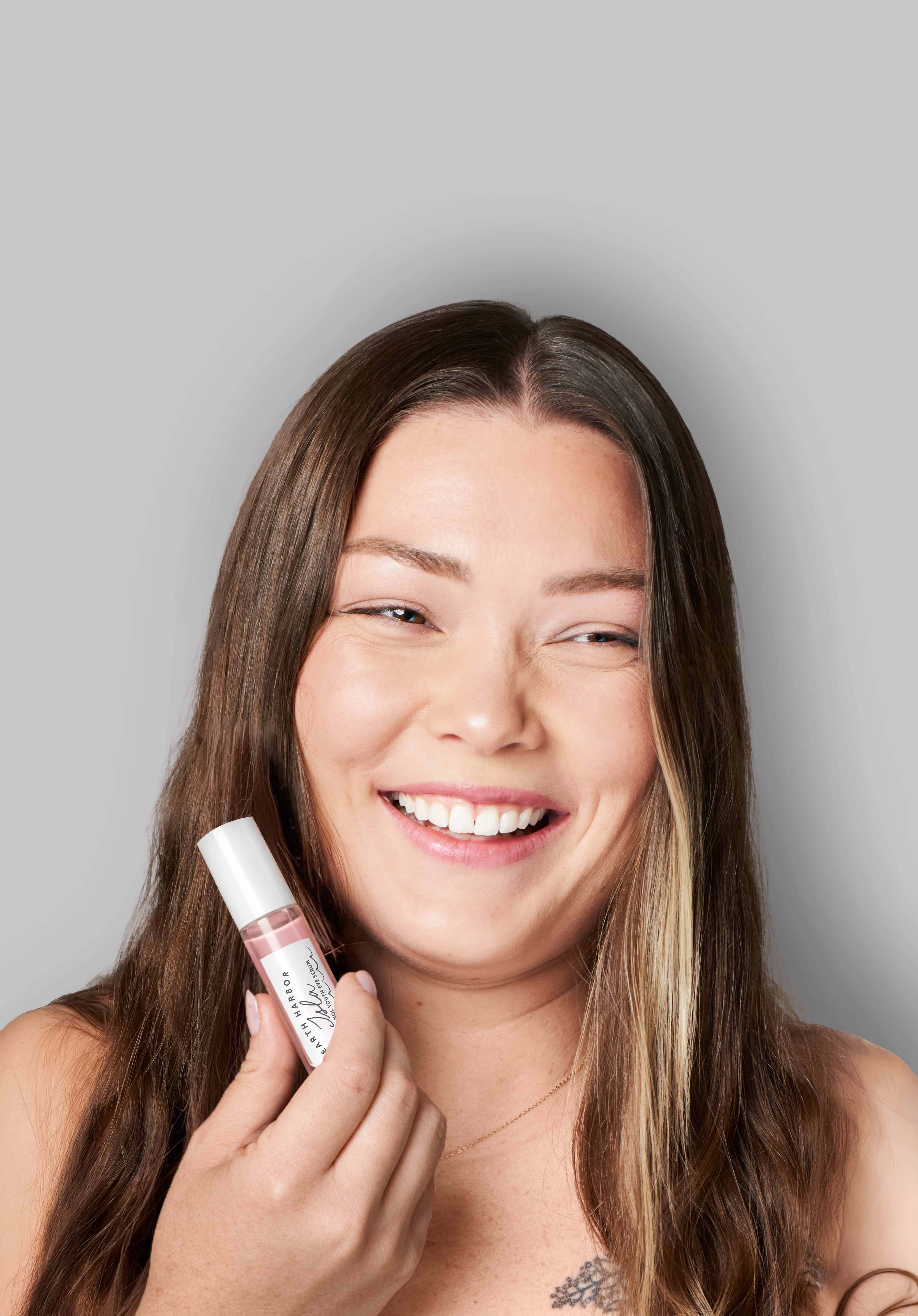 Woman smiling while holding a pink Isla
serum bottle near her face​